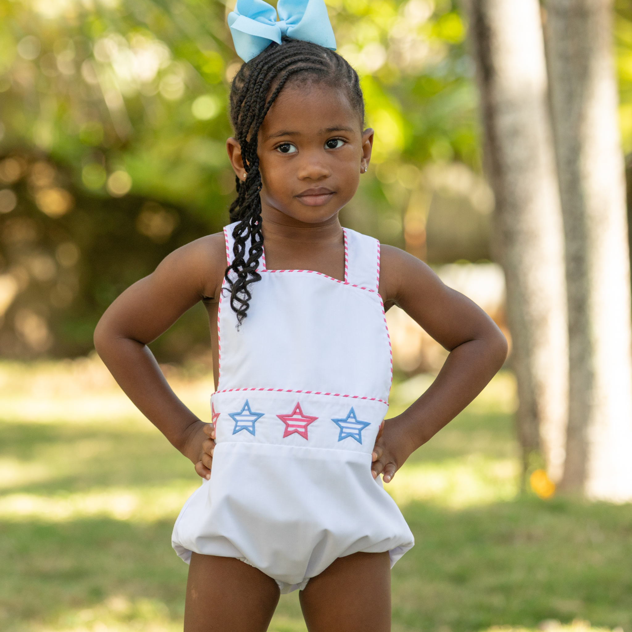 Henry Duvall unisex baby sunsuit in white with red and blue star appliqué and criss cross straps, classic patriotic outfit for Memorial Day, 4th of July, and summer occasions