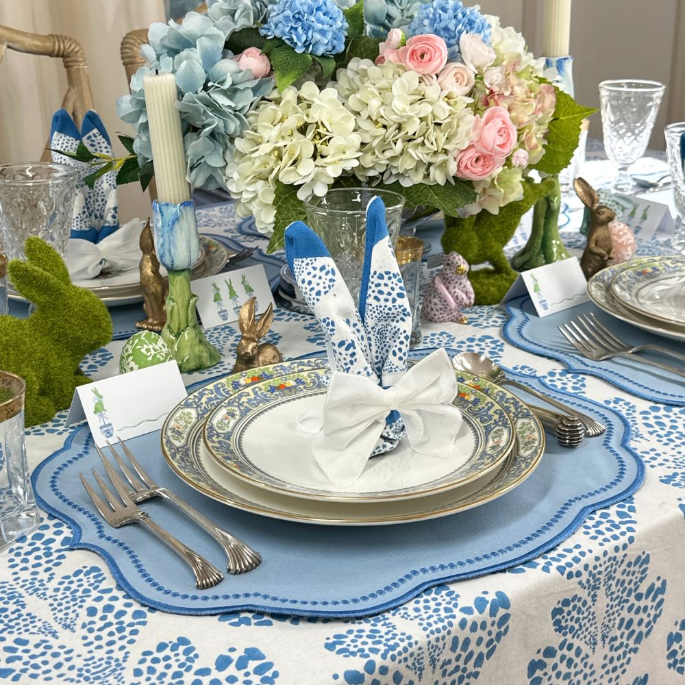 Easter table setting with floral centerpieces, bunny decorations, and patterned tablecloth.