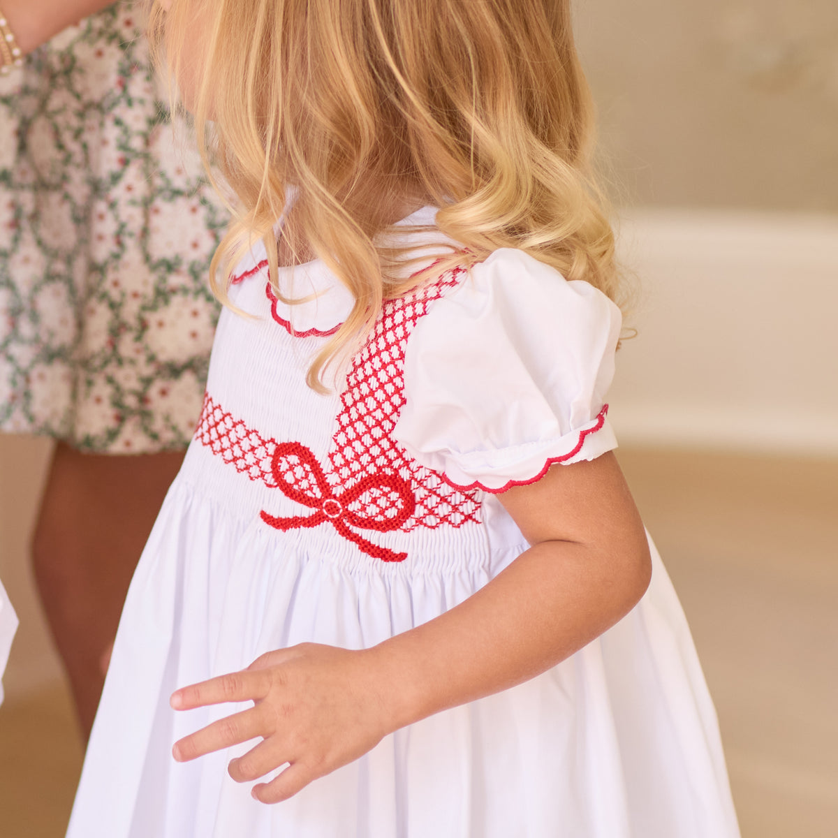 White short sleeve girls' holiday dress with red bow smocking across the chest, Peter Pan collar, and piped cuffs, classic Henry Duvall Eloise Dress for Christmas and winter family gatherings