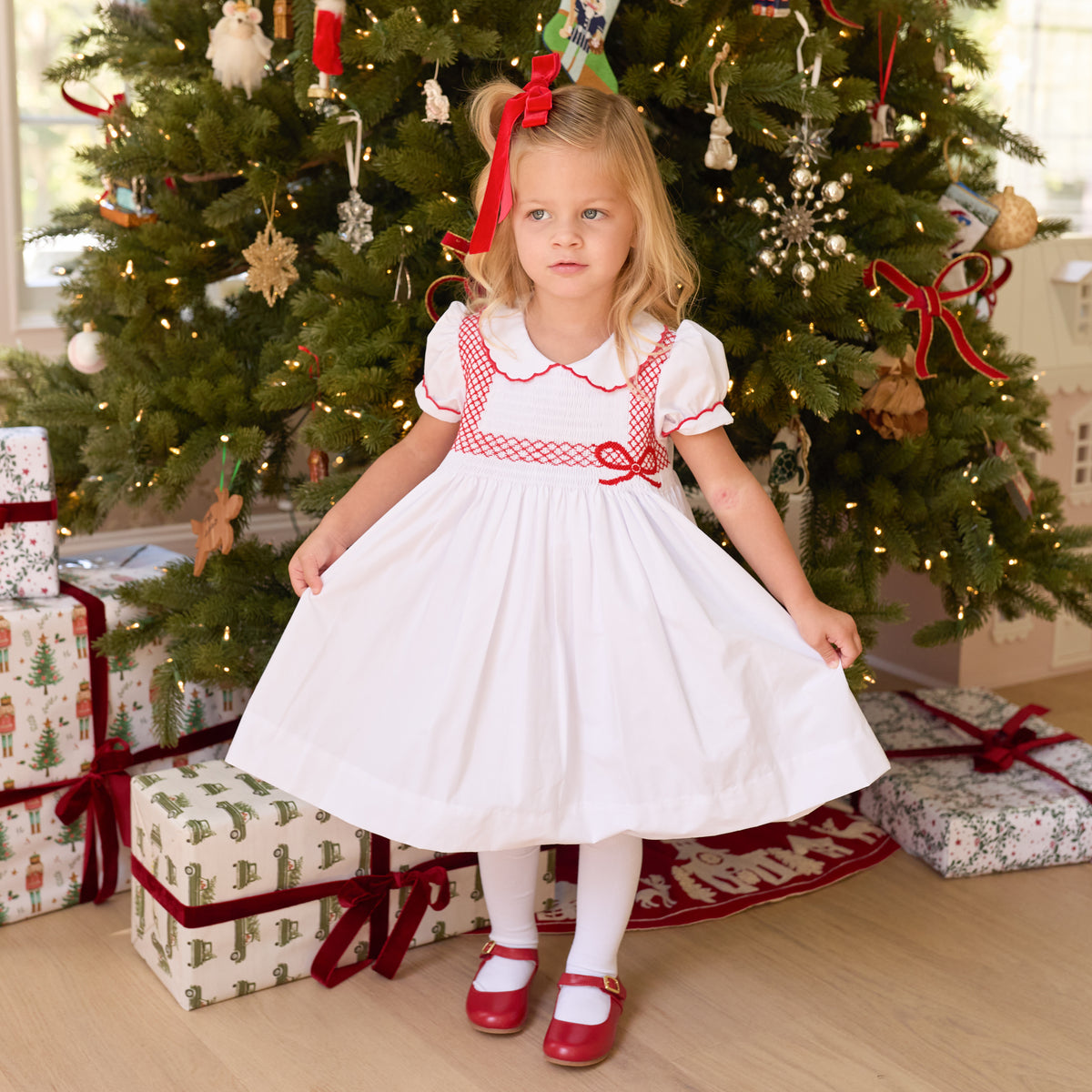 White short sleeve girls' holiday dress with red bow smocking across the chest, Peter Pan collar, and piped cuffs, classic Henry Duvall Eloise Dress for Christmas and winter family gatherings