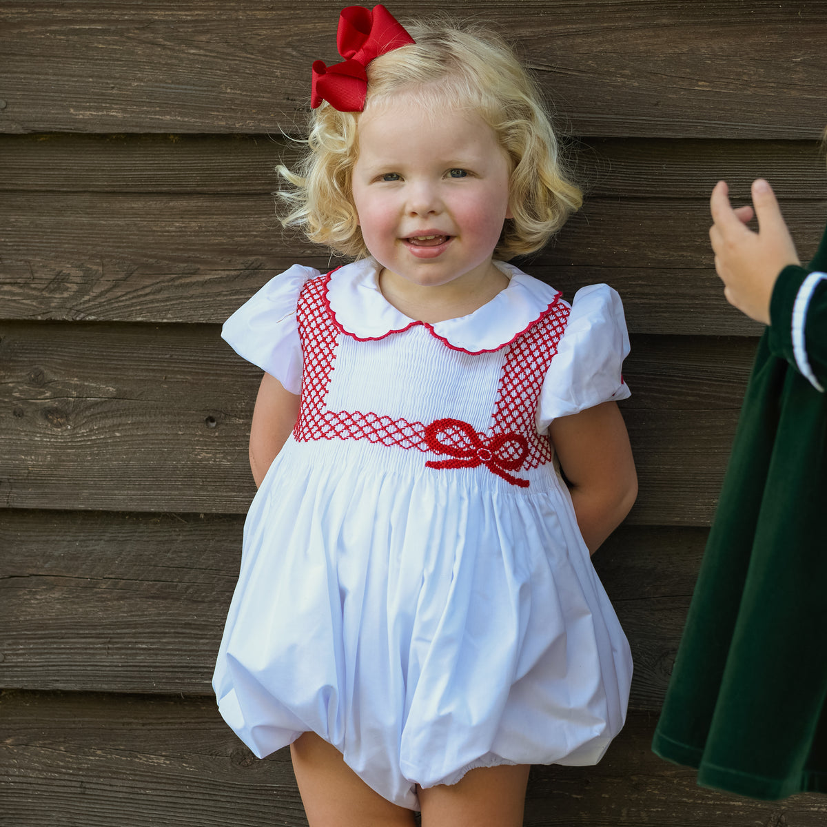 White short sleeve baby girl holiday bubble with red smocked bows, Peter Pan collar, and piped cuffs, classic Eloise Bubble by Henry Duvall for Christmas and winter celebrations
