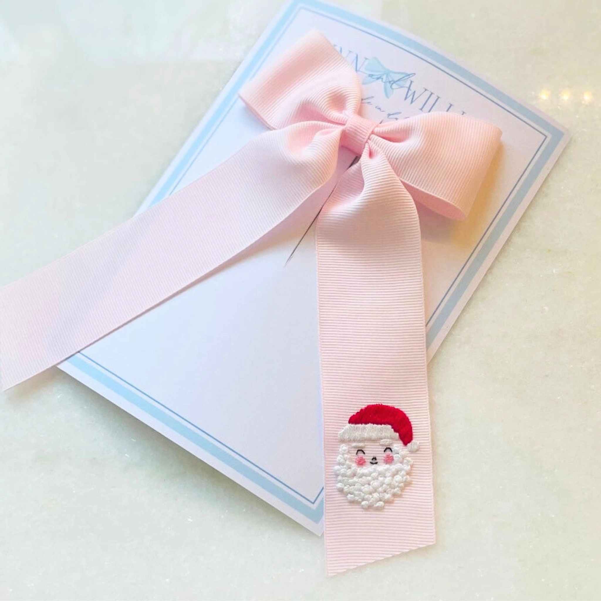Pink ribbon with a Santa Claus design on a white card