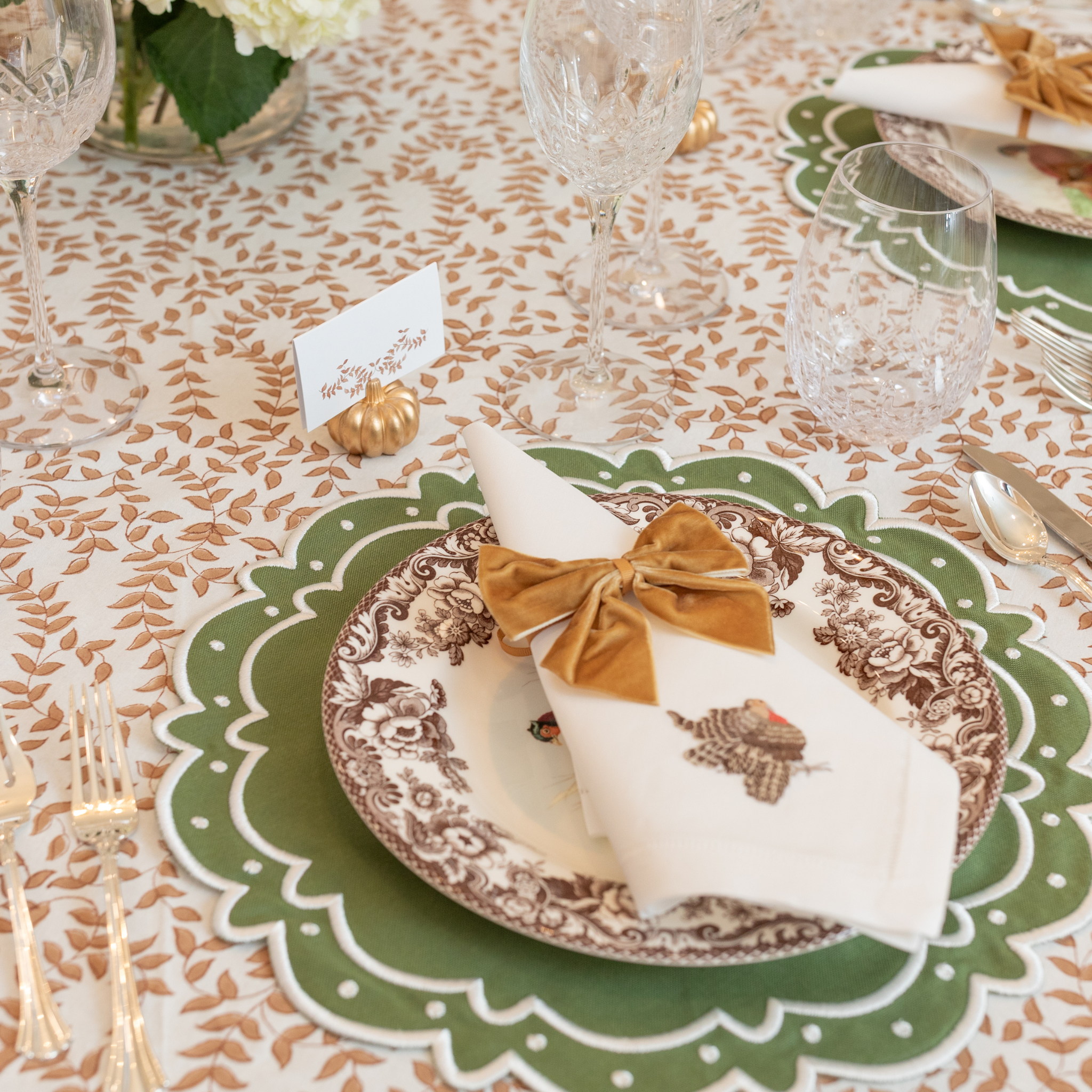 Folded tent-style Thanksgiving place cards with brown woodland leaf motif, matching fall tablecloths and Thanksgiving tabletop decor