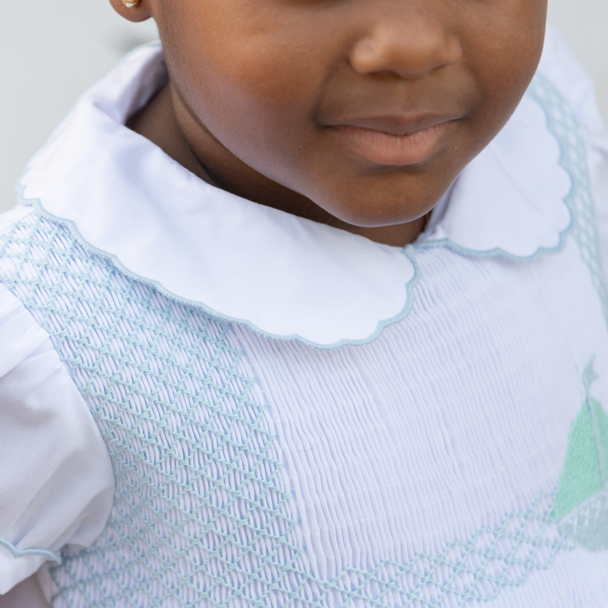 Henry Duvall Eloise Dress in white cotton with Bailey’s Bay Blue trim and hand-smocked sailboats, classic heirloom baby girl summer outfit with scalloped Peter Pan collar