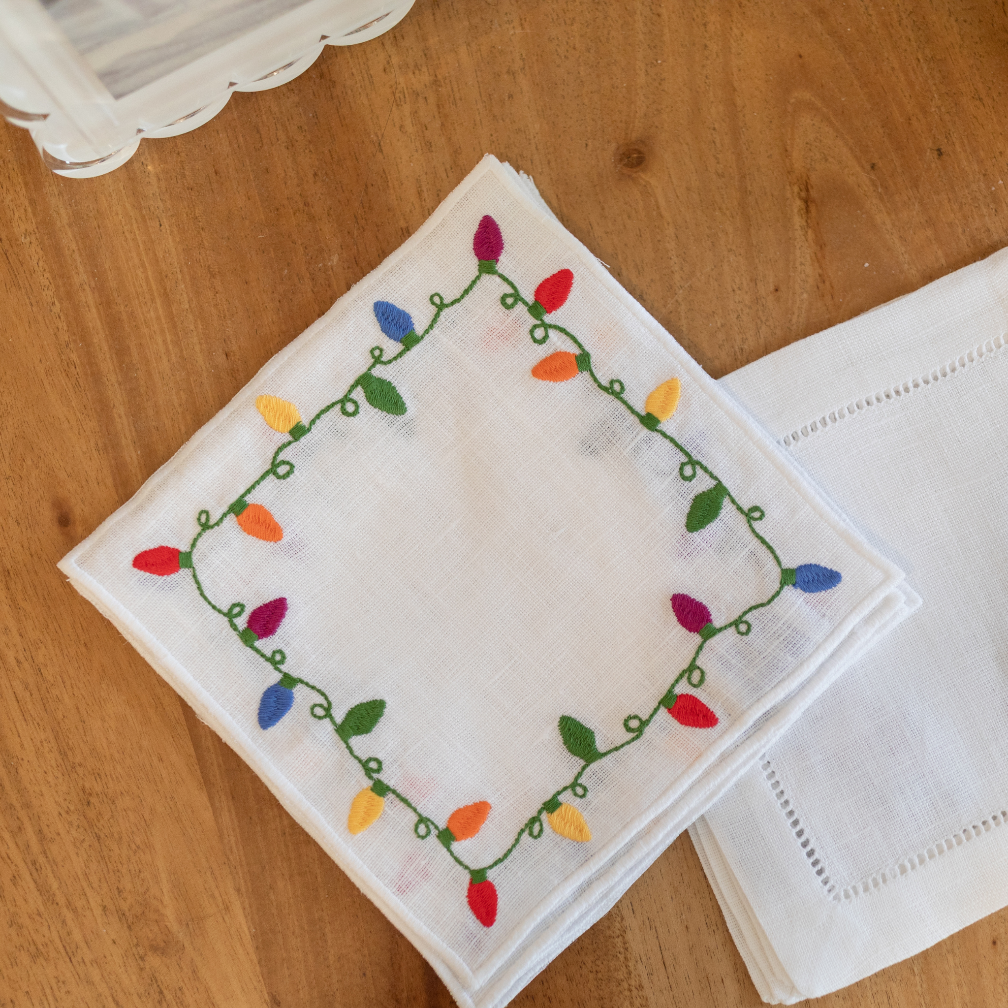 Set of four white linen cocktail napkins with embroidered multicolor Christmas lights framing each edge