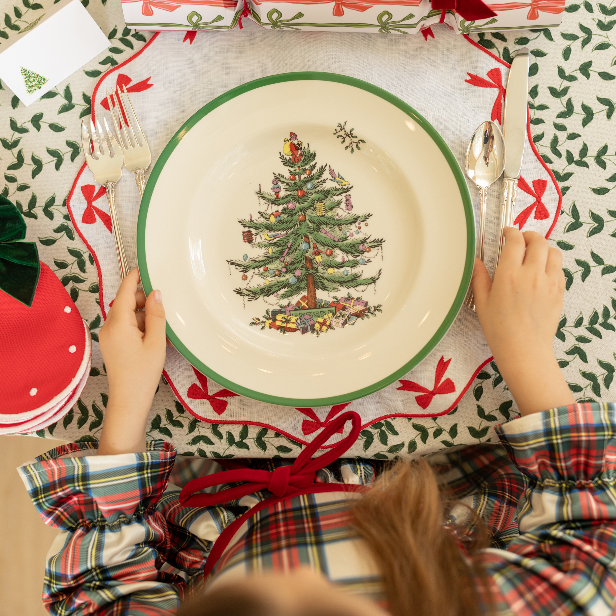 White linen placemat with scalloped edges and red embroidered bows, styled for holiday tabletop decor.