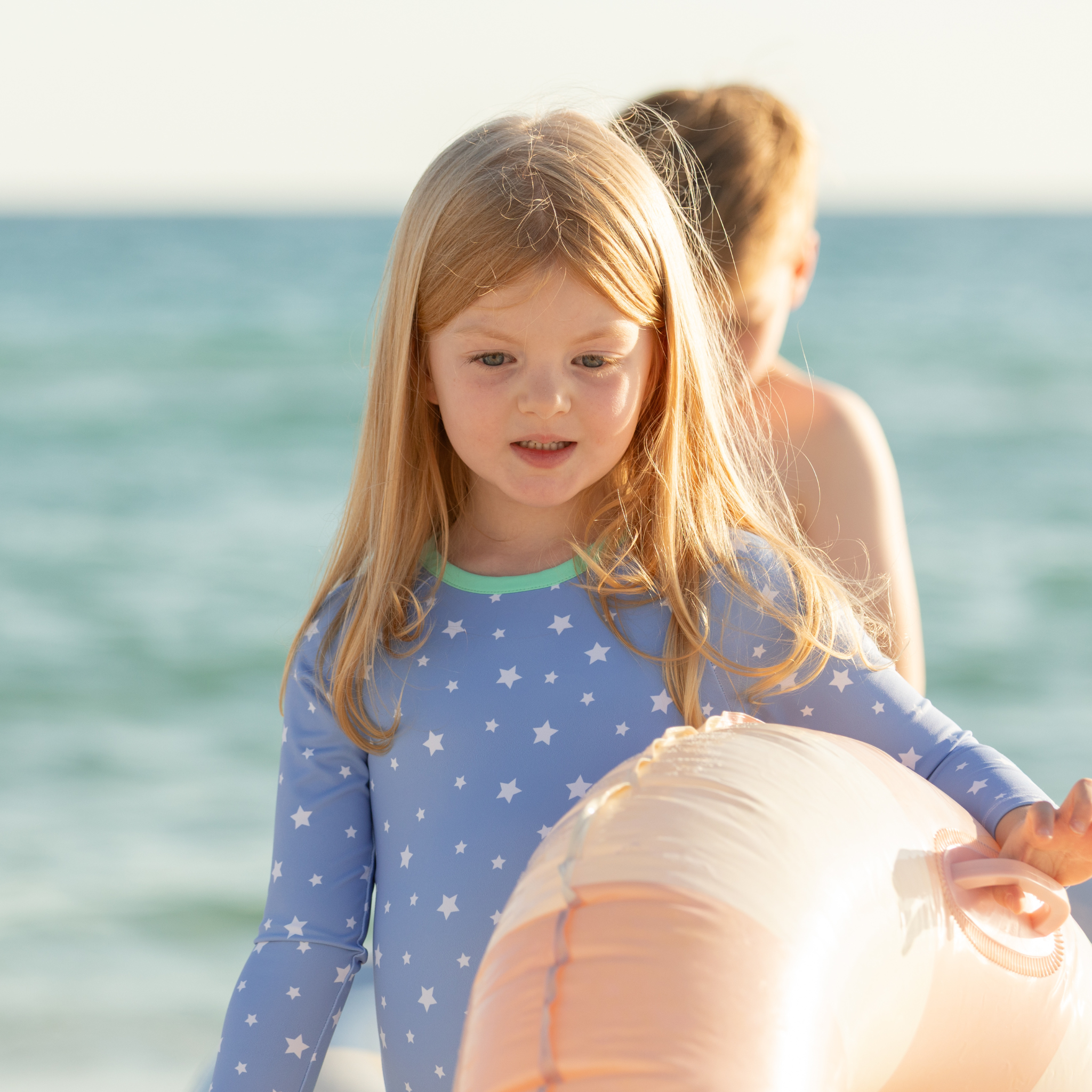 Girls’ long sleeve rashguard one piece swimsuit in Seaside Seersucker with UPF 50+ and scalloped open back, perfect for summer or beach vacations by Henry Duvall.