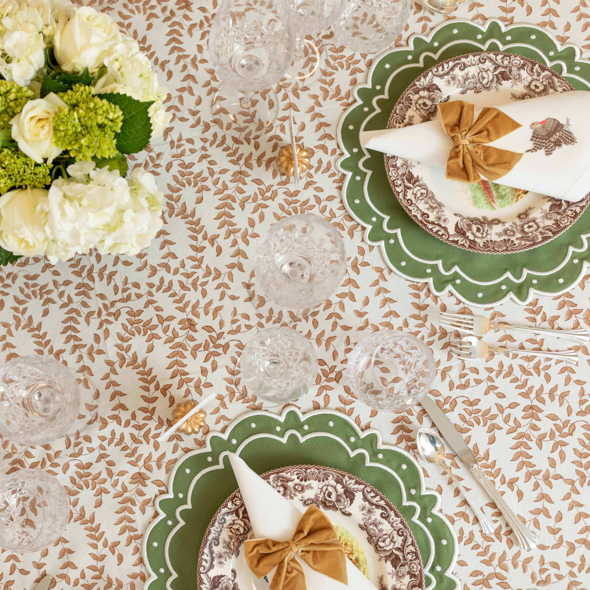 Golden velvet bow napkin ties styled for a Thanksgiving table setting with brown floral china and green scalloped placemats from Henry Duvall.