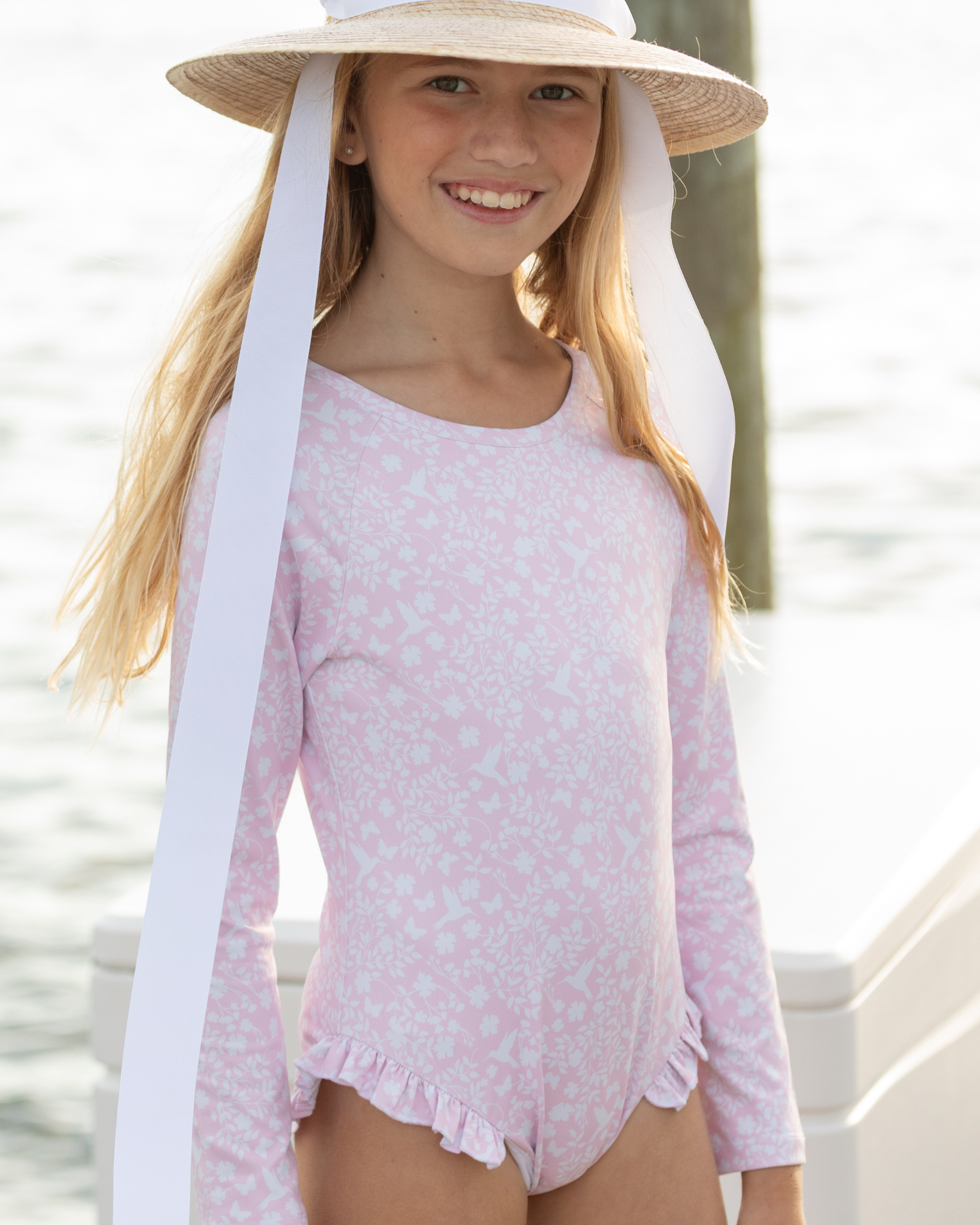 Girls’ long sleeve rashguard one piece swimsuit in Seaside Seersucker with UPF 50+ and scalloped open back, perfect for summer or beach vacations by Henry Duvall.