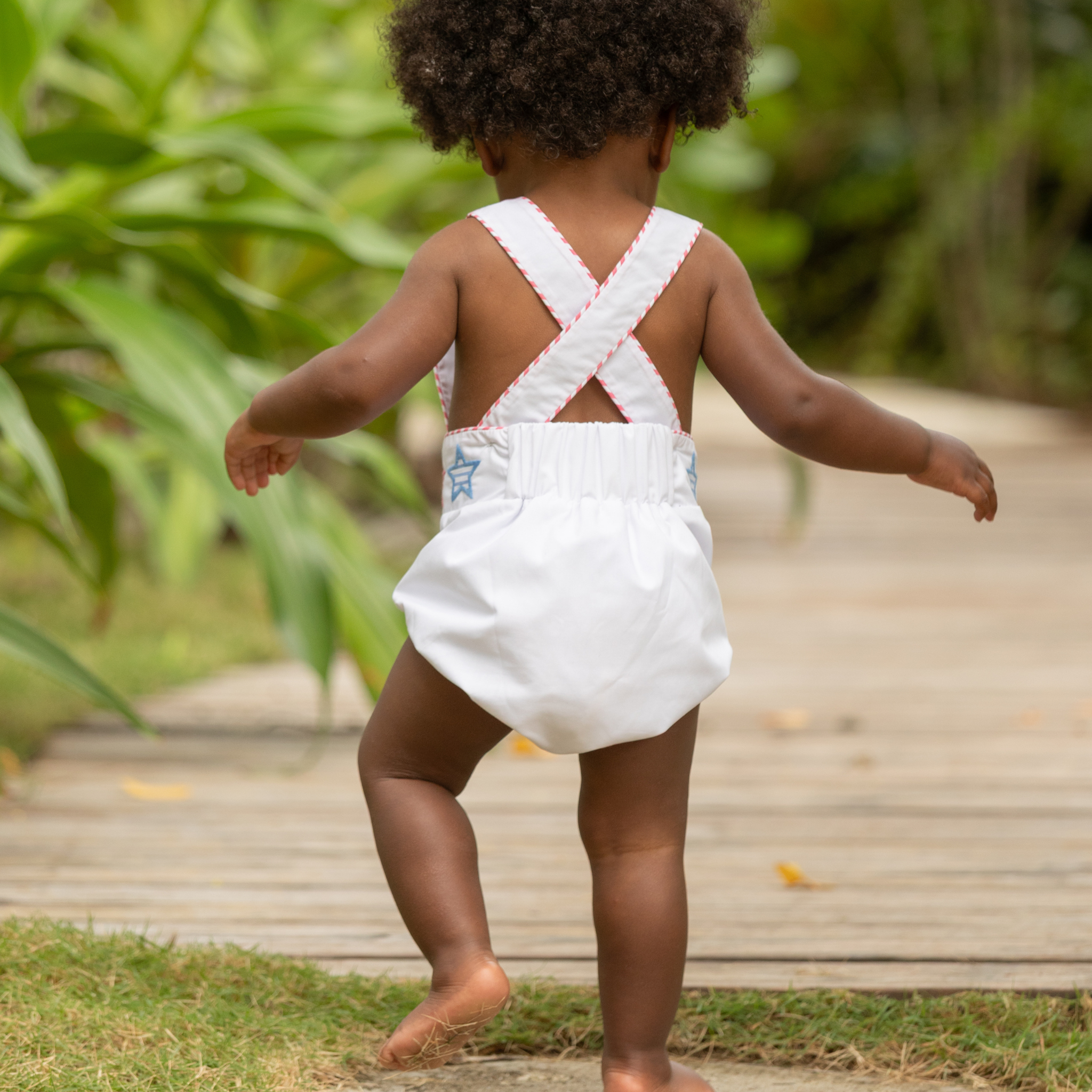 Henry Duvall unisex baby sunsuit in white with red and blue star appliqué and criss cross straps, classic patriotic outfit for Memorial Day, 4th of July, and summer occasions