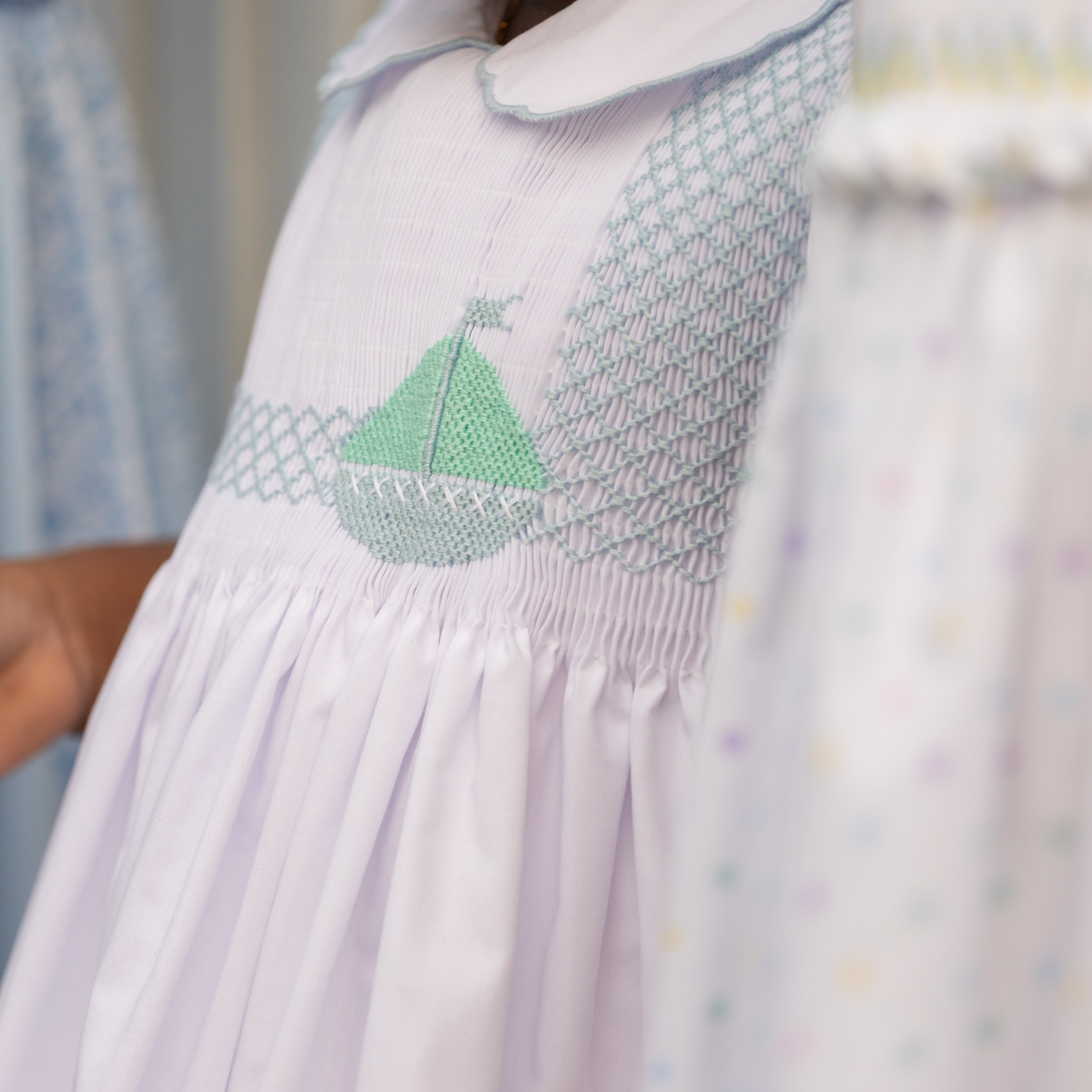 Henry Duvall Eloise Dress in white cotton with Bailey’s Bay Blue trim and hand-smocked sailboats, classic heirloom baby girl summer outfit with scalloped Peter Pan collar