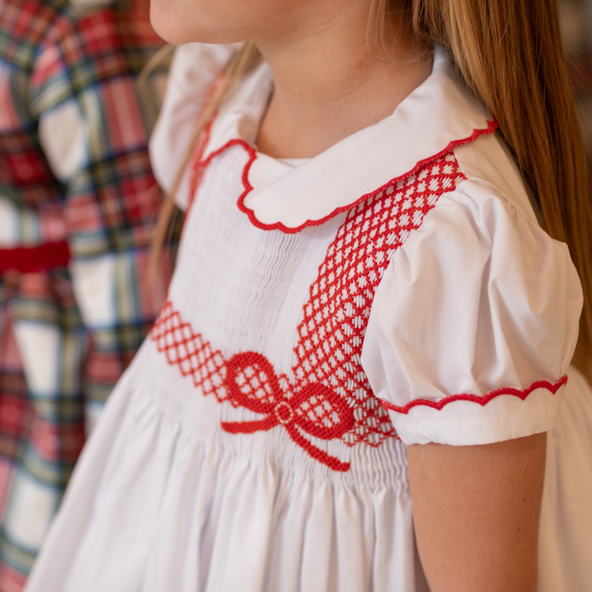 White short sleeve girls' holiday dress with red bow smocking across the chest, Peter Pan collar, and piped cuffs, classic Henry Duvall Eloise Dress for Christmas and winter family gatherings