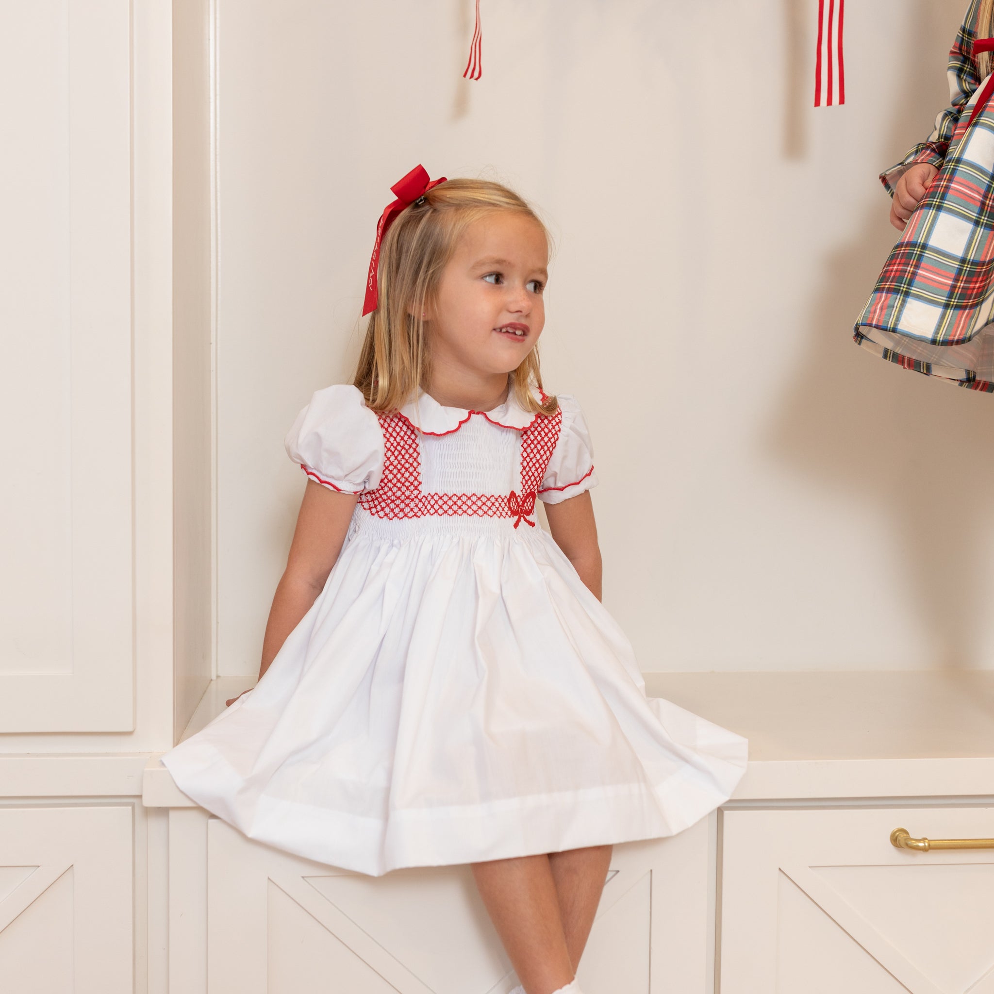 White short sleeve girls' holiday dress with red bow smocking across the chest, Peter Pan collar, and piped cuffs, classic Henry Duvall Eloise Dress for Christmas and winter family gatherings