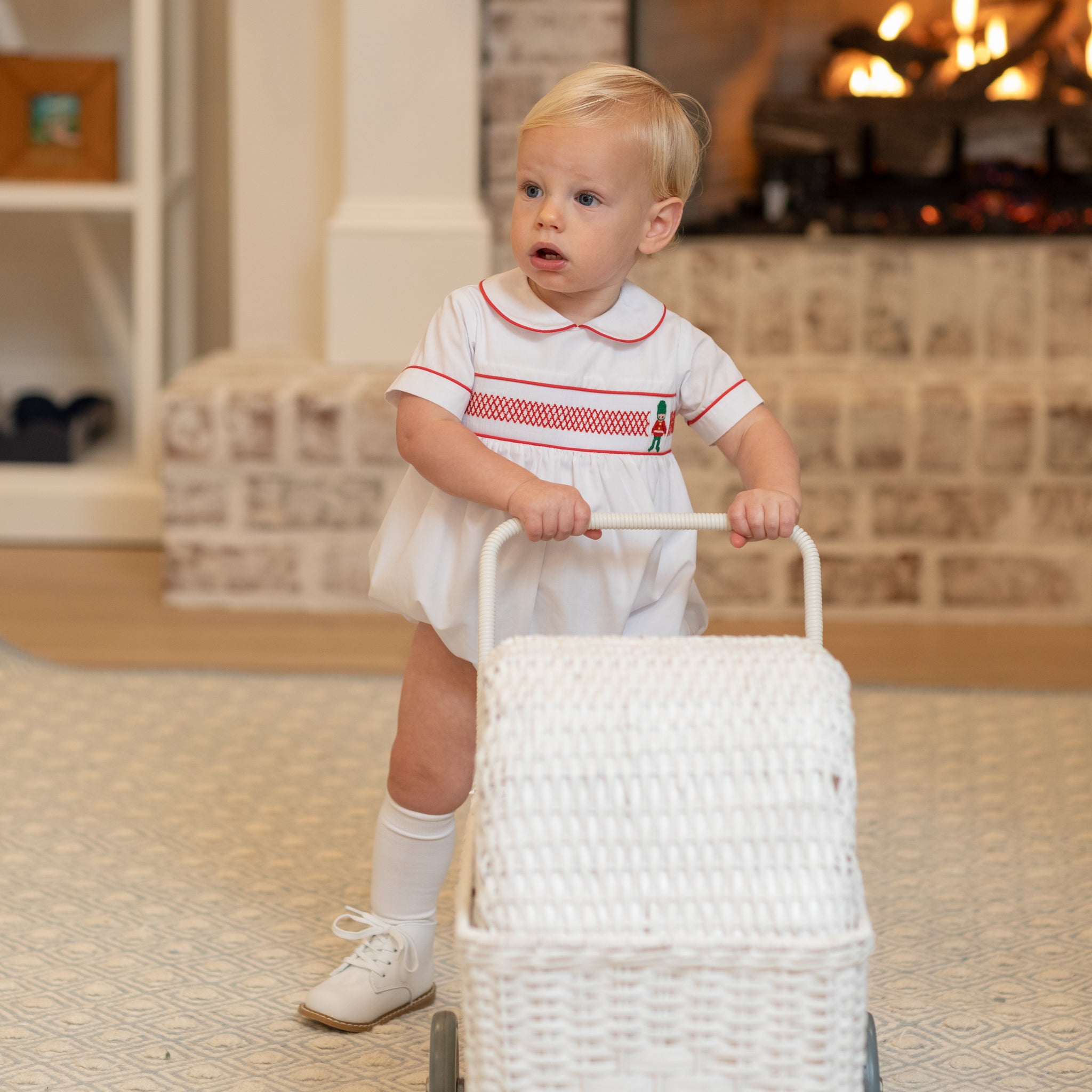 White baby boy holiday bubble with red toy soldier smocking and Peter Pan collar, Henry Duvall's Charlie Bubble in cotton poplin for Christmas celebrations