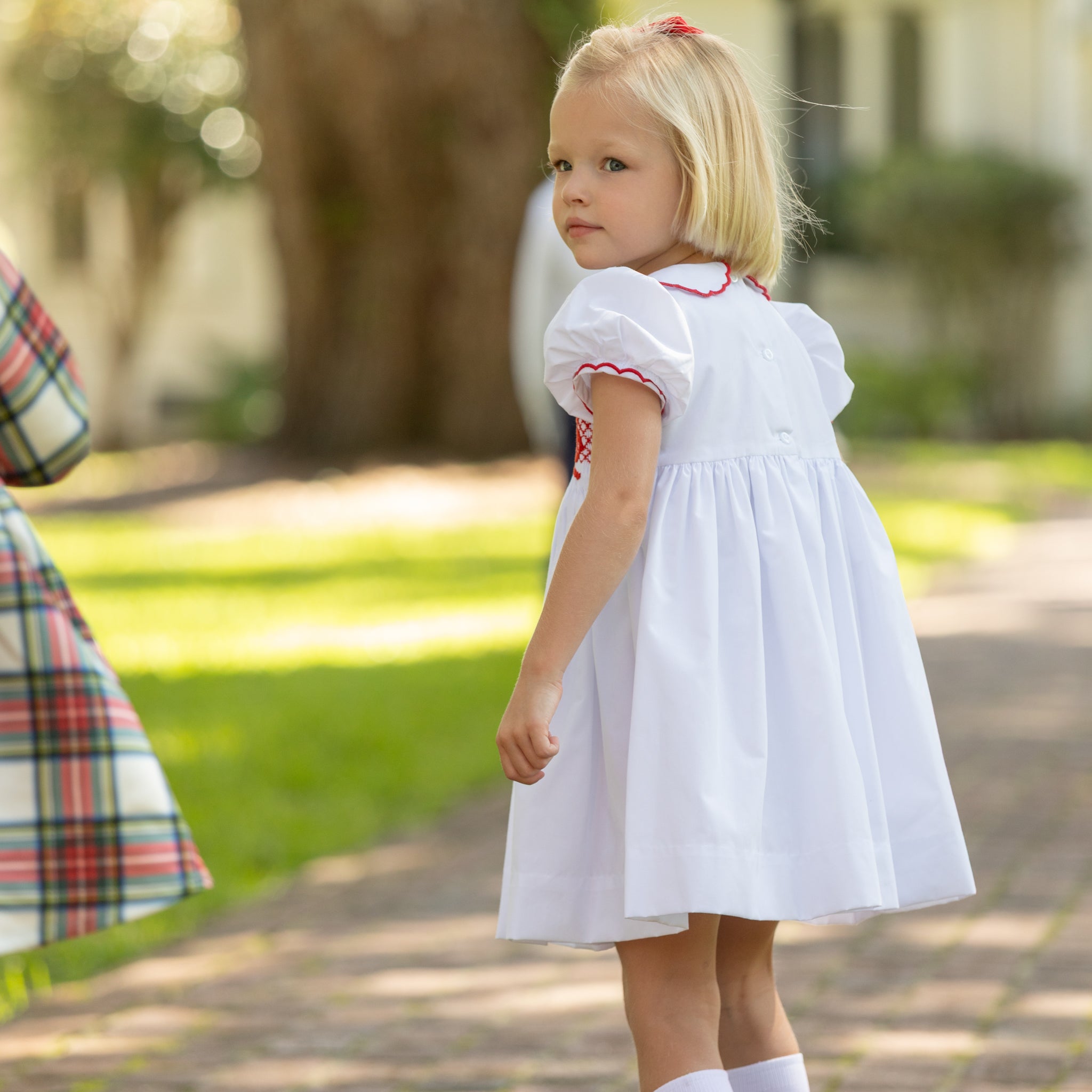 White short sleeve girls' holiday dress with red bow smocking across the chest, Peter Pan collar, and piped cuffs, classic Henry Duvall Eloise Dress for Christmas and winter family gatherings