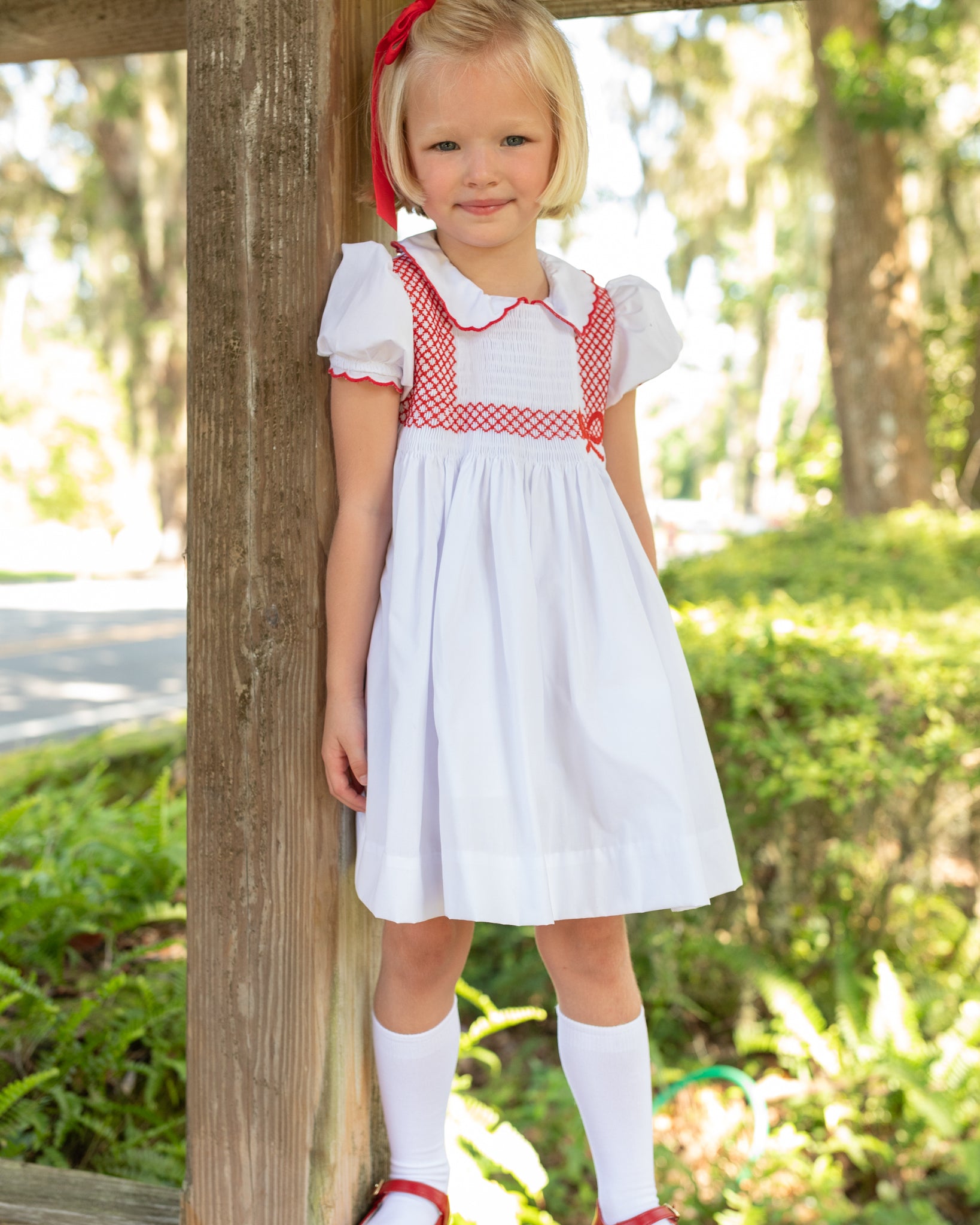 White short sleeve girls' holiday dress with red bow smocking across the chest, Peter Pan collar, and piped cuffs, classic Henry Duvall Eloise Dress for Christmas and winter family gatherings