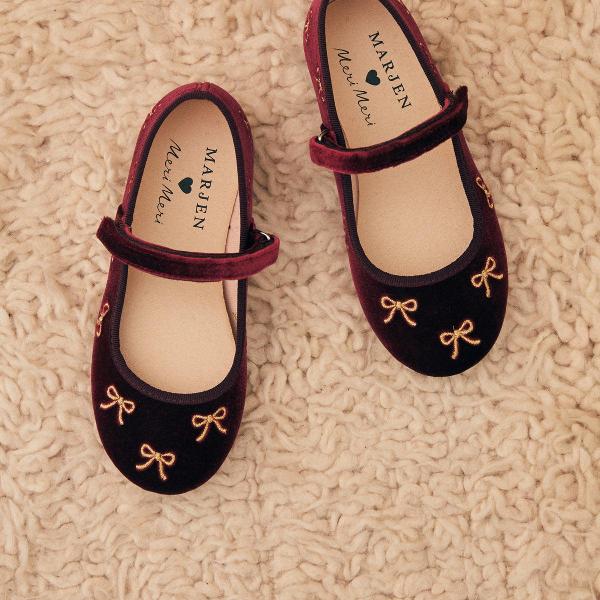 Meri Meri x Marjen Bowie burgundy velvet Mary Jane with gold bow embroidery, pair on a cream rug