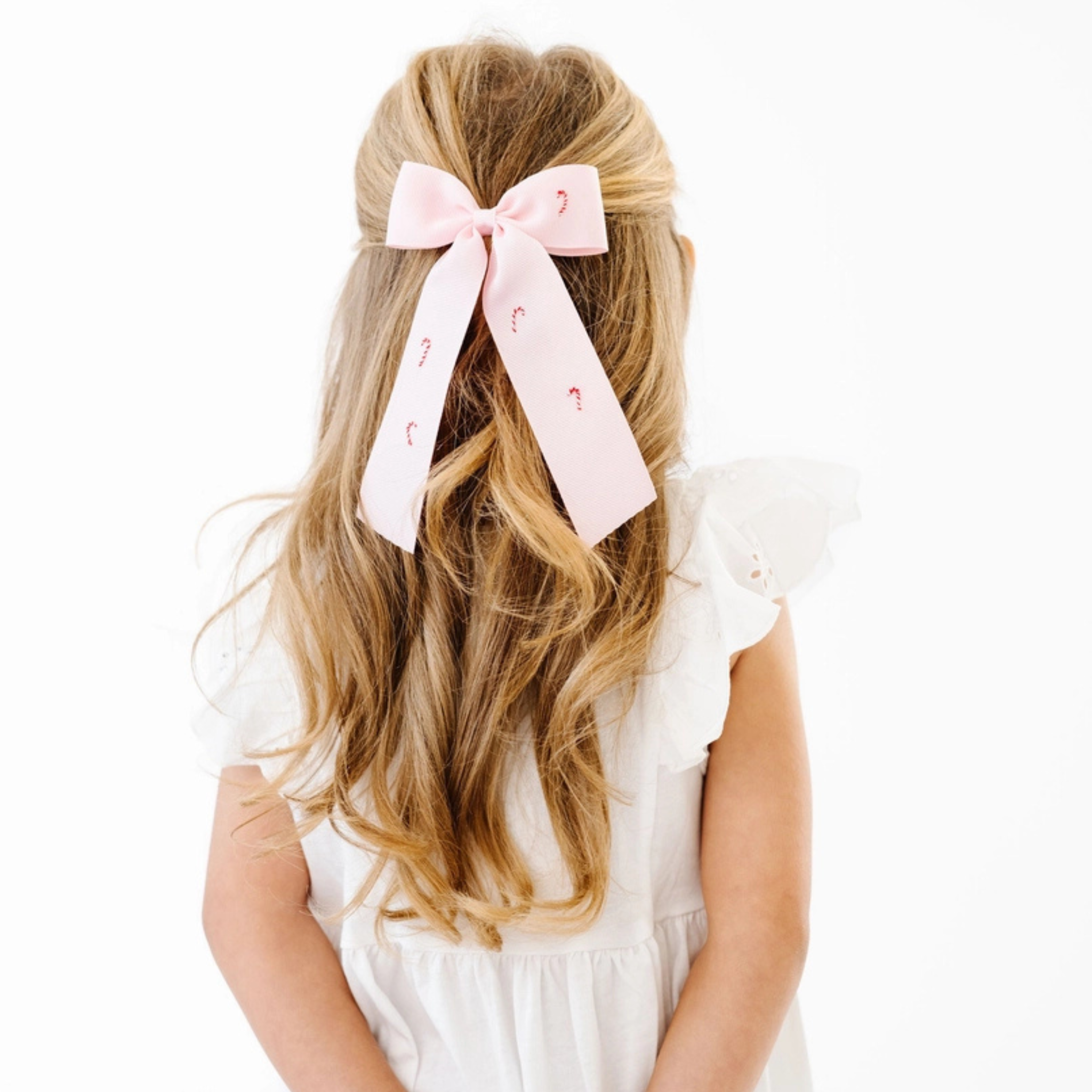 Young girl with long blonde hair wearing a pink bow with letters, against a white background