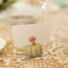 Watercolor Thanksgiving place card featuring a pumpkin illustration, displayed in a pale green pumpkin holder on a patterned fall tablecloth.