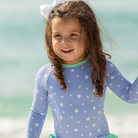 Girls’ long sleeve rashguard one piece swimsuit in Seaside Seersucker with UPF 50+ and scalloped open back, perfect for summer or beach vacations by Henry Duvall.