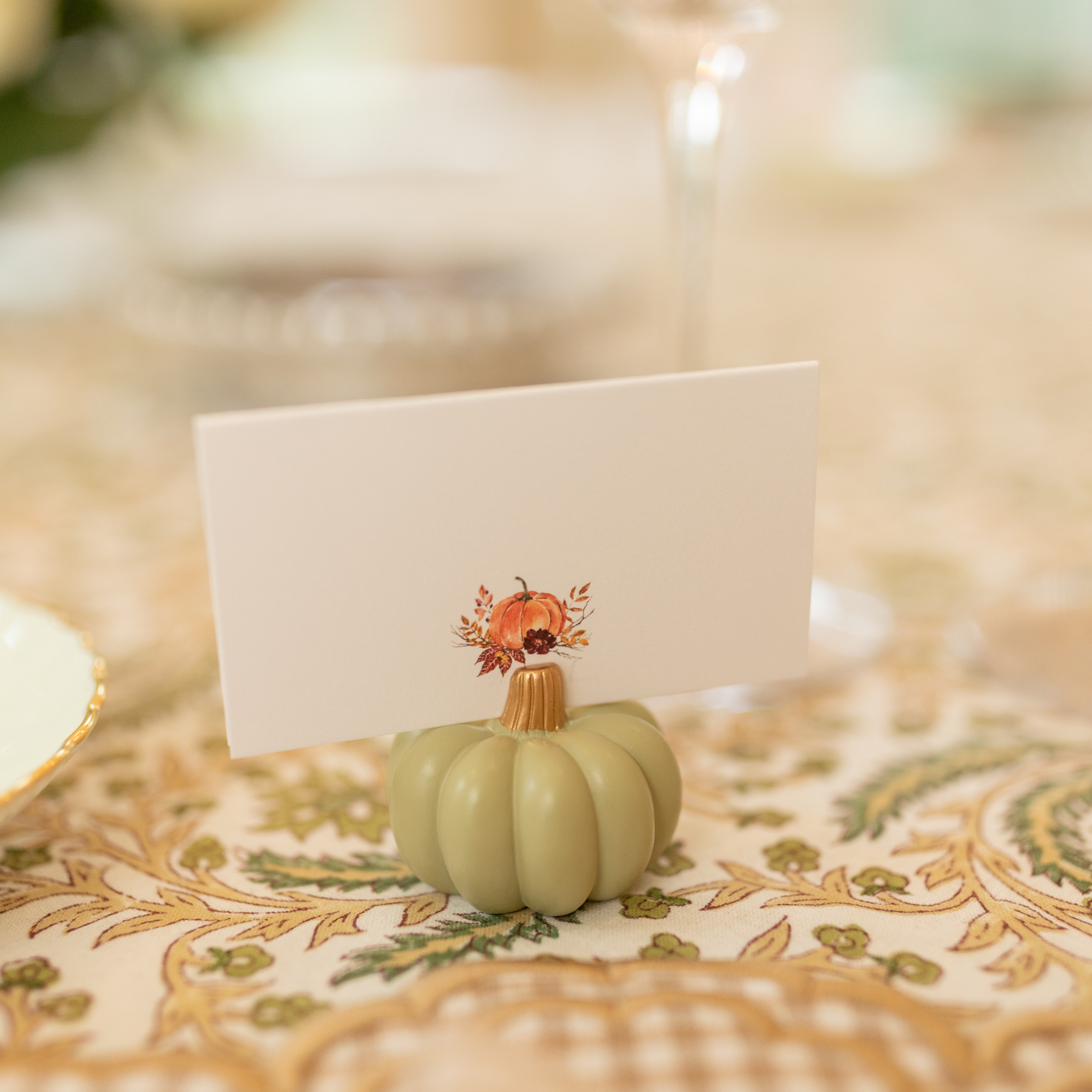 Sage green pumpkin-shaped place card holder on a fall-themed table setting.