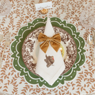Golden velvet bow napkin ties styled for a Thanksgiving table setting with brown floral china and green scalloped placemats from Henry Duvall.