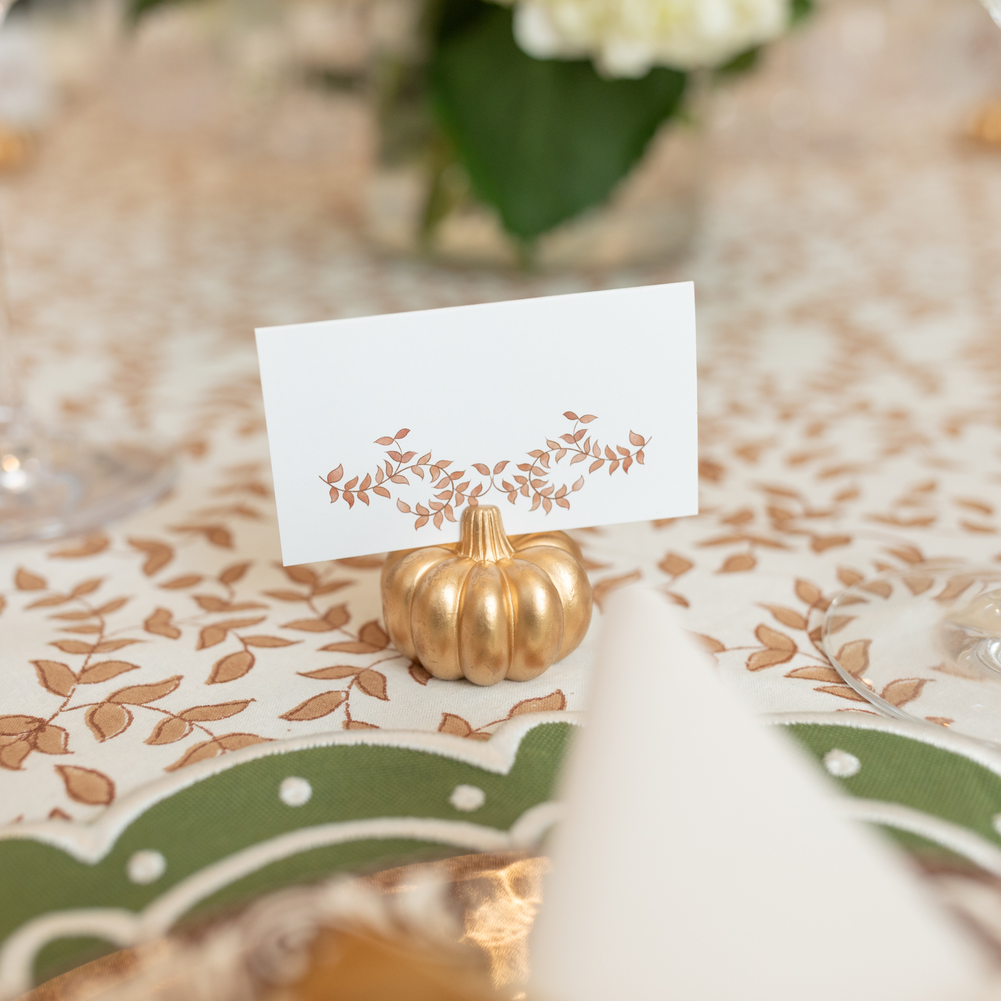 Folded tent-style Thanksgiving place cards with brown woodland leaf motif, matching fall tablecloths and Thanksgiving tabletop decor
