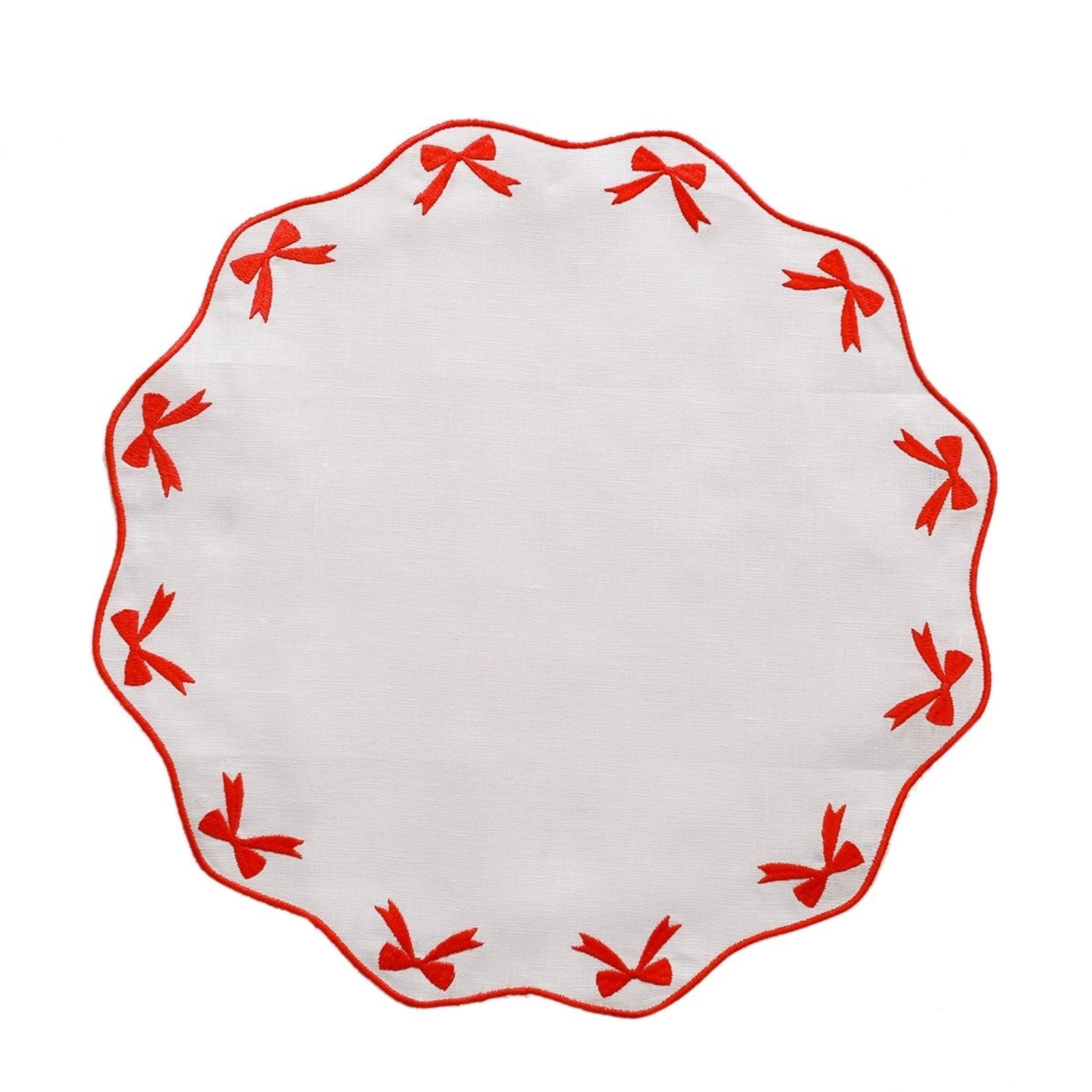 White linen placemat with scalloped edges and red embroidered bows, styled for holiday tabletop decor.