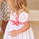White short sleeve girls' holiday dress with red bow smocking across the chest, Peter Pan collar, and piped cuffs, classic Henry Duvall Eloise Dress for Christmas and winter family gatherings