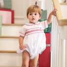 White baby boy holiday bubble with red toy soldier smocking and Peter Pan collar, Henry Duvall's Charlie Bubble in cotton poplin for Christmas celebrations