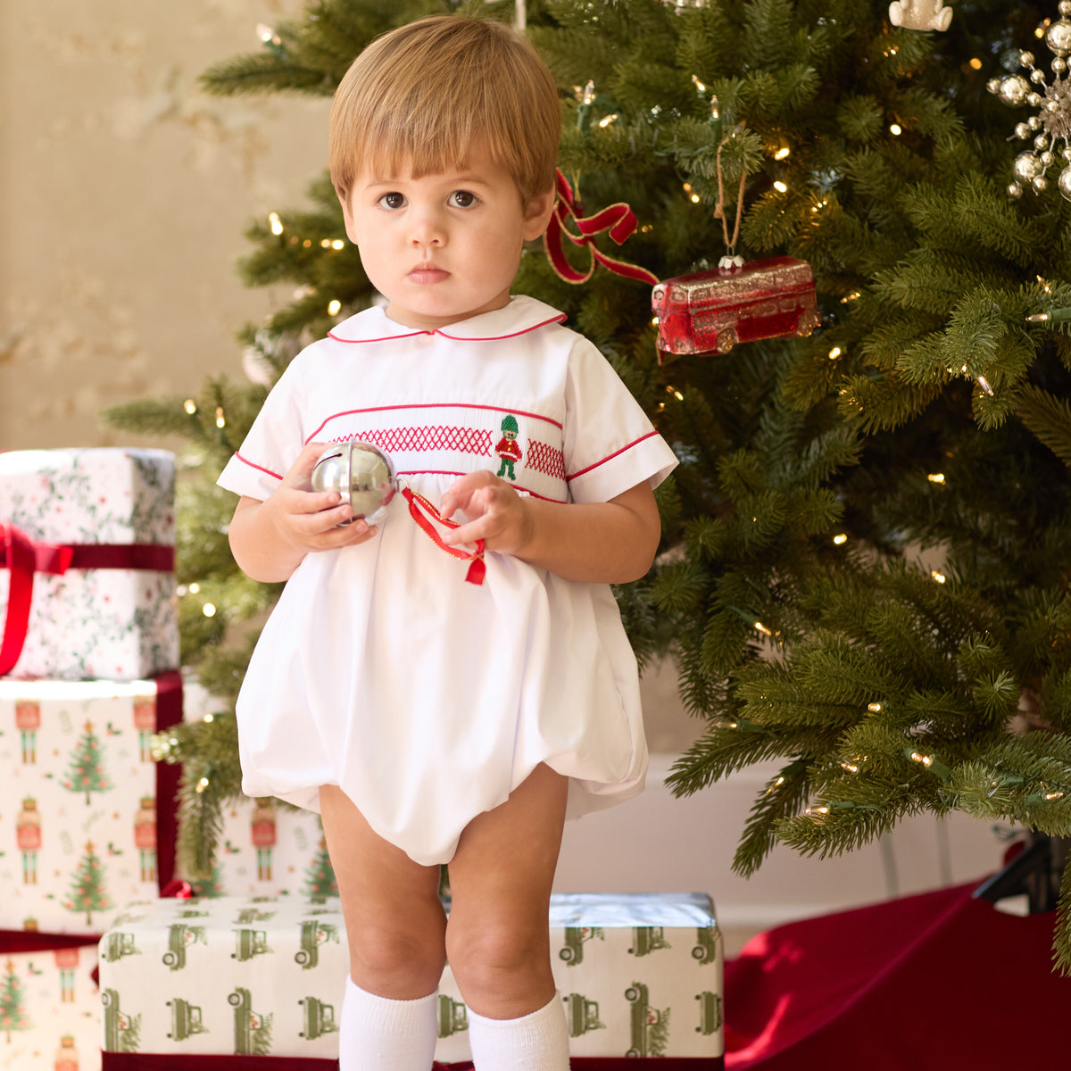 White baby boy holiday bubble with red toy soldier smocking and Peter Pan collar, Henry Duvall's Charlie Bubble in cotton poplin for Christmas celebrations