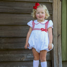 White short sleeve baby girl holiday bubble with red smocked bows, Peter Pan collar, and piped cuffs, classic Eloise Bubble by Henry Duvall for Christmas and winter celebrations