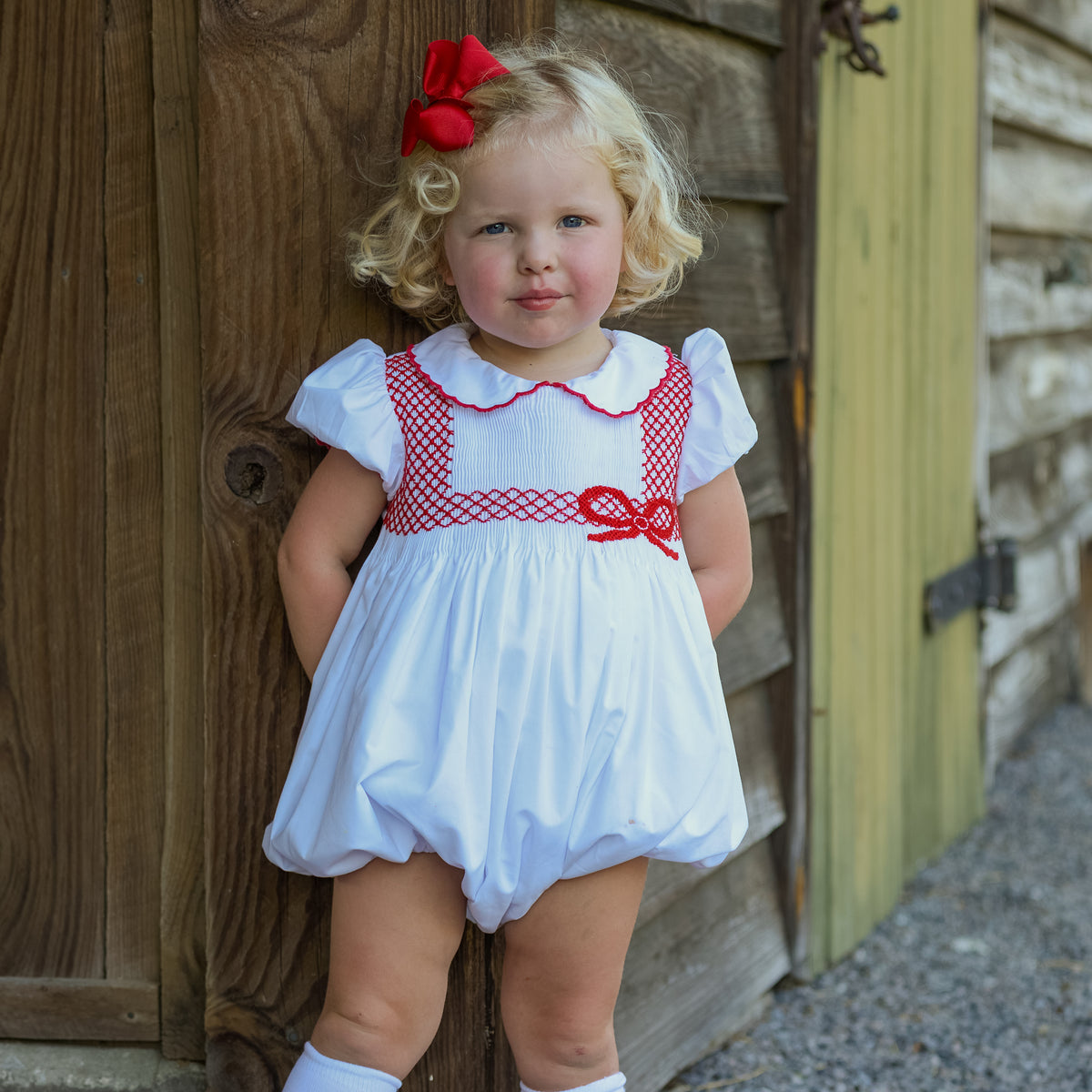 White short sleeve baby girl holiday bubble with red smocked bows, Peter Pan collar, and piped cuffs, classic Eloise Bubble by Henry Duvall for Christmas and winter celebrations