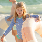 Girls’ long sleeve rashguard one piece swimsuit in Seaside Seersucker with UPF 50+ and scalloped open back, perfect for summer or beach vacations by Henry Duvall.