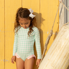 Girls’ long sleeve rashguard one piece swimsuit in Seaside Seersucker with UPF 50+ and scalloped open back, perfect for summer or beach vacations by Henry Duvall.