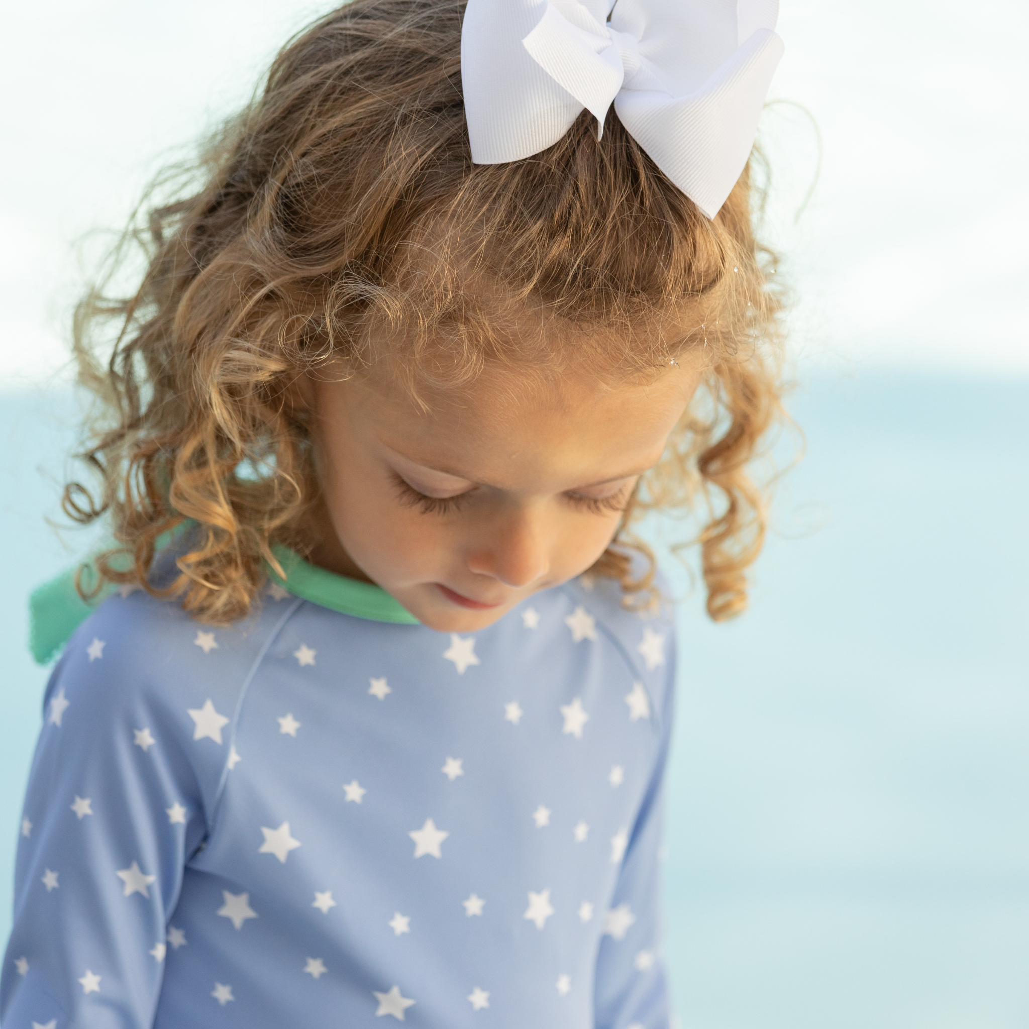 Girls’ long sleeve rashguard one piece swimsuit in Seaside Seersucker with UPF 50+ and scalloped open back, perfect for summer or beach vacations by Henry Duvall.