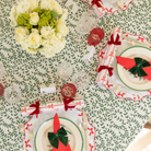 Holiday tablescape with Flying Sheep Country green leaf block-printed tablecloth, red ribbon details, holiday crackers, crystal glassware, and a white floral centerpiece