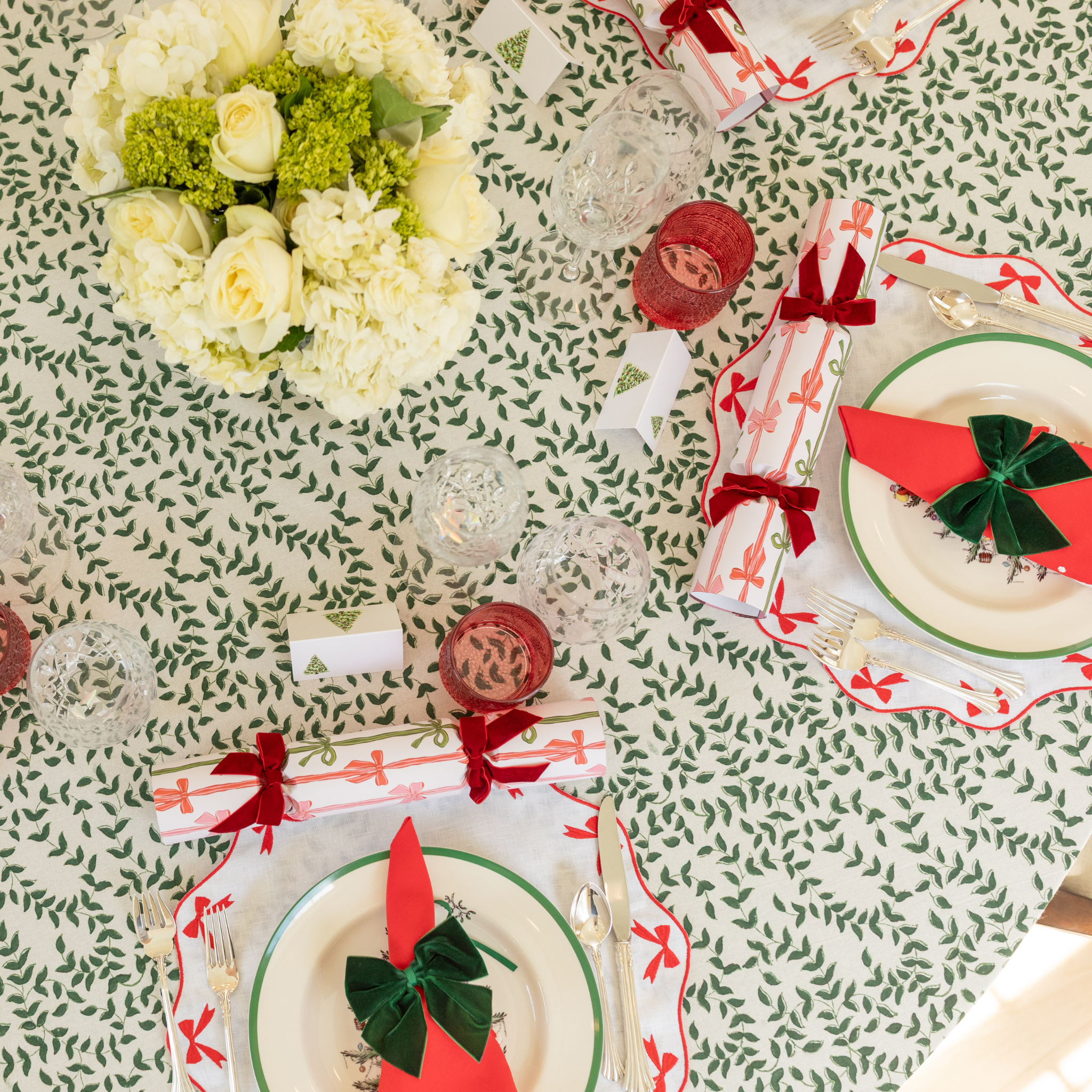 Holiday tablescape with Flying Sheep Country green leaf block-printed tablecloth, red ribbon details, holiday crackers, crystal glassware, and a white floral centerpiece