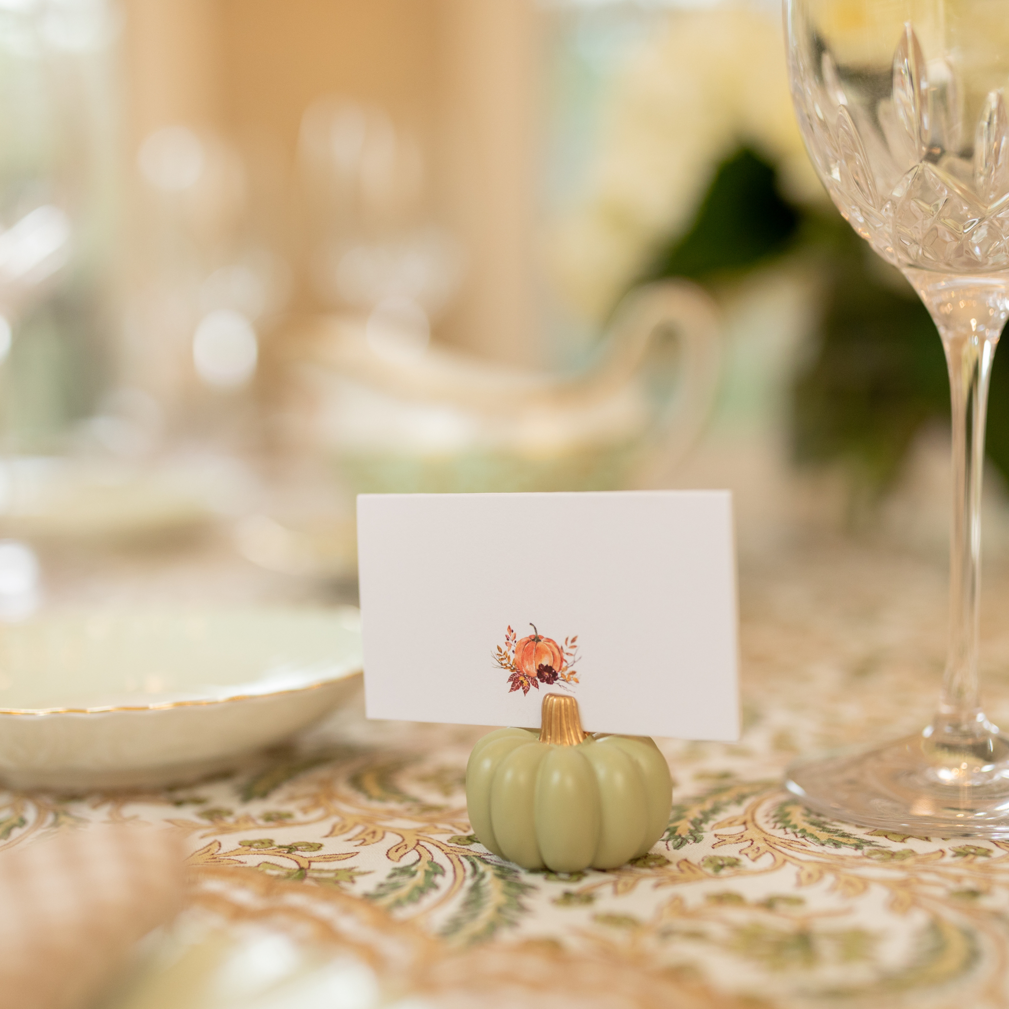 Sage green pumpkin-shaped place card holder on a fall-themed table setting.