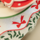 White linen placemat with scalloped edges and red embroidered bows, styled for holiday tabletop decor.