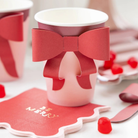 Red and pink paper party cup with a large red paper bow attached to the front, perfect for festive holiday gatherings.