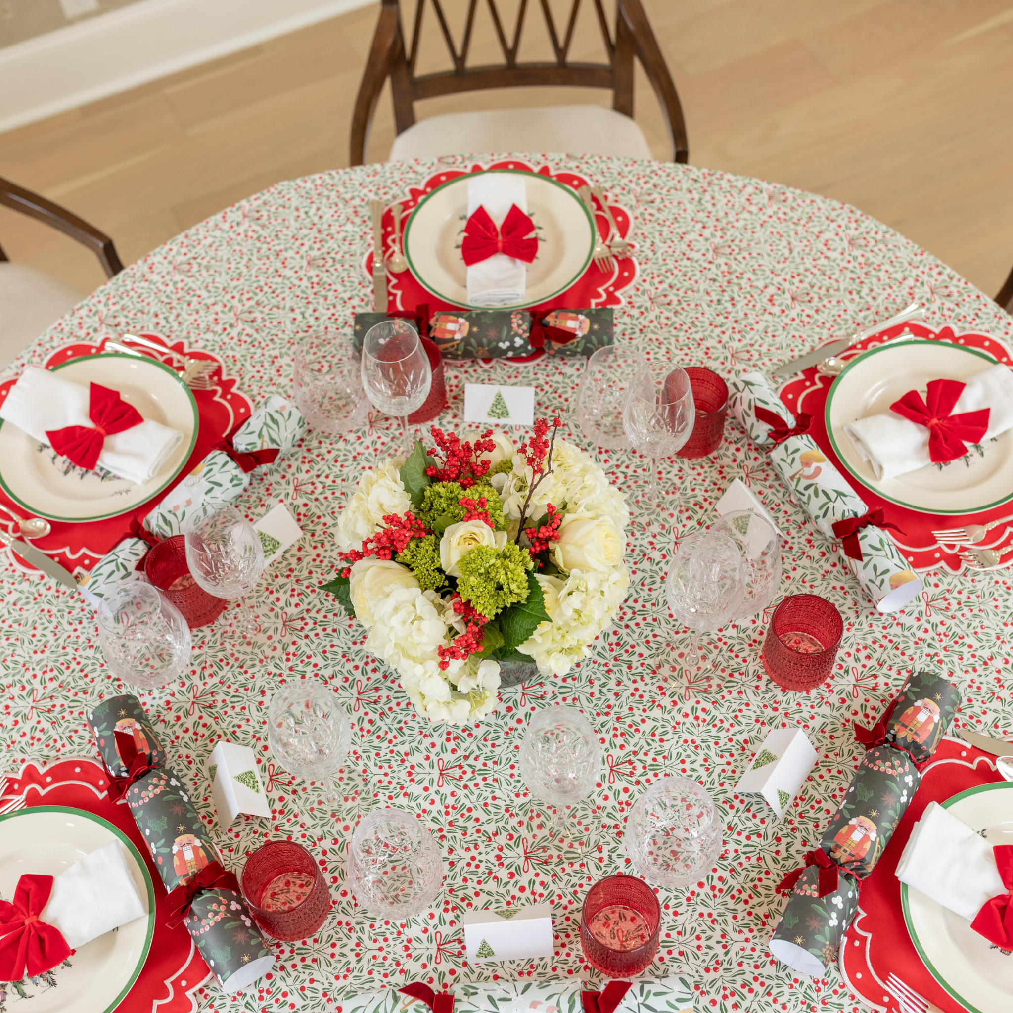 Red velvet bow napkin ties on white napkins, styled on a festive holiday table with holly tablecloth and scalloped placemats – perfect for Christmas entertaining and seasonal celebrations.
