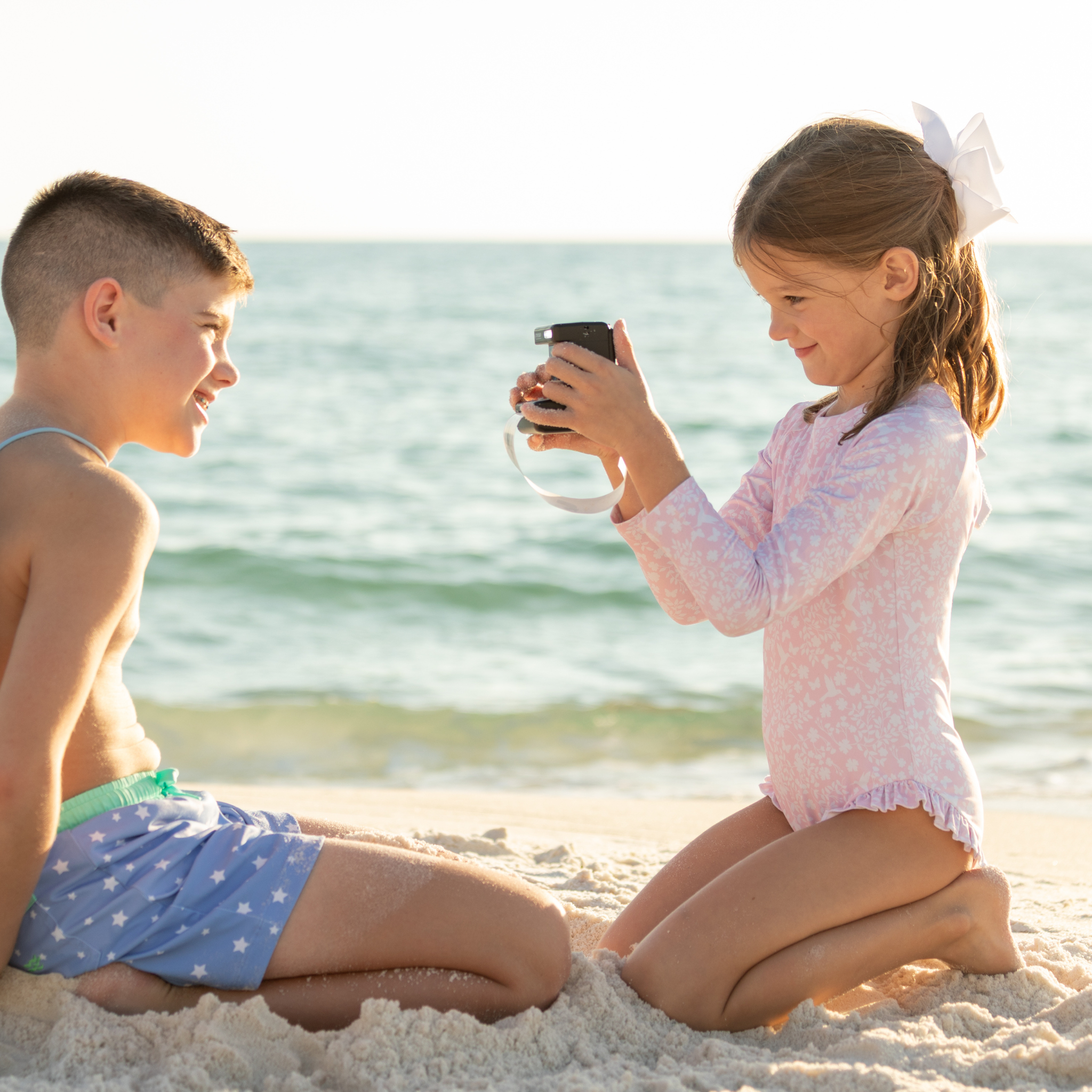 Girls’ long sleeve rashguard one piece swimsuit in Seaside Seersucker with UPF 50+ and scalloped open back, perfect for summer or beach vacations by Henry Duvall.