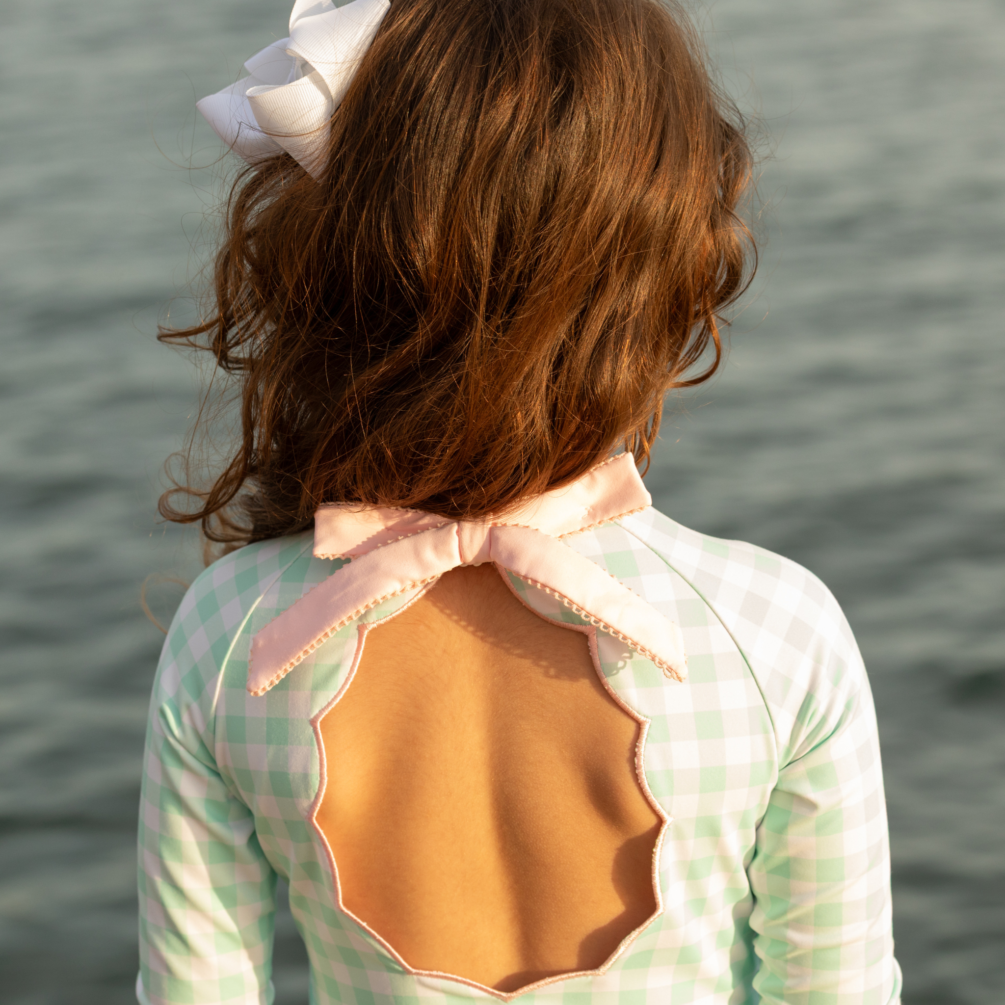 Girls’ long sleeve rashguard one piece swimsuit in Seaside Seersucker with UPF 50+ and scalloped open back, perfect for summer or beach vacations by Henry Duvall.