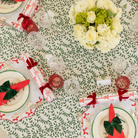 White linen placemat with scalloped edges and red embroidered bows, styled for holiday tabletop decor.