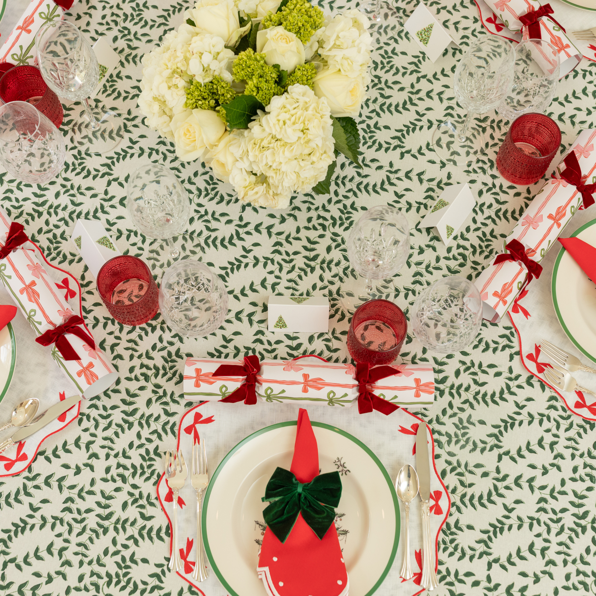 Holiday tablescape with Flying Sheep Country green leaf block-printed tablecloth, red ribbon details, holiday crackers, crystal glassware, and a white floral centerpiece