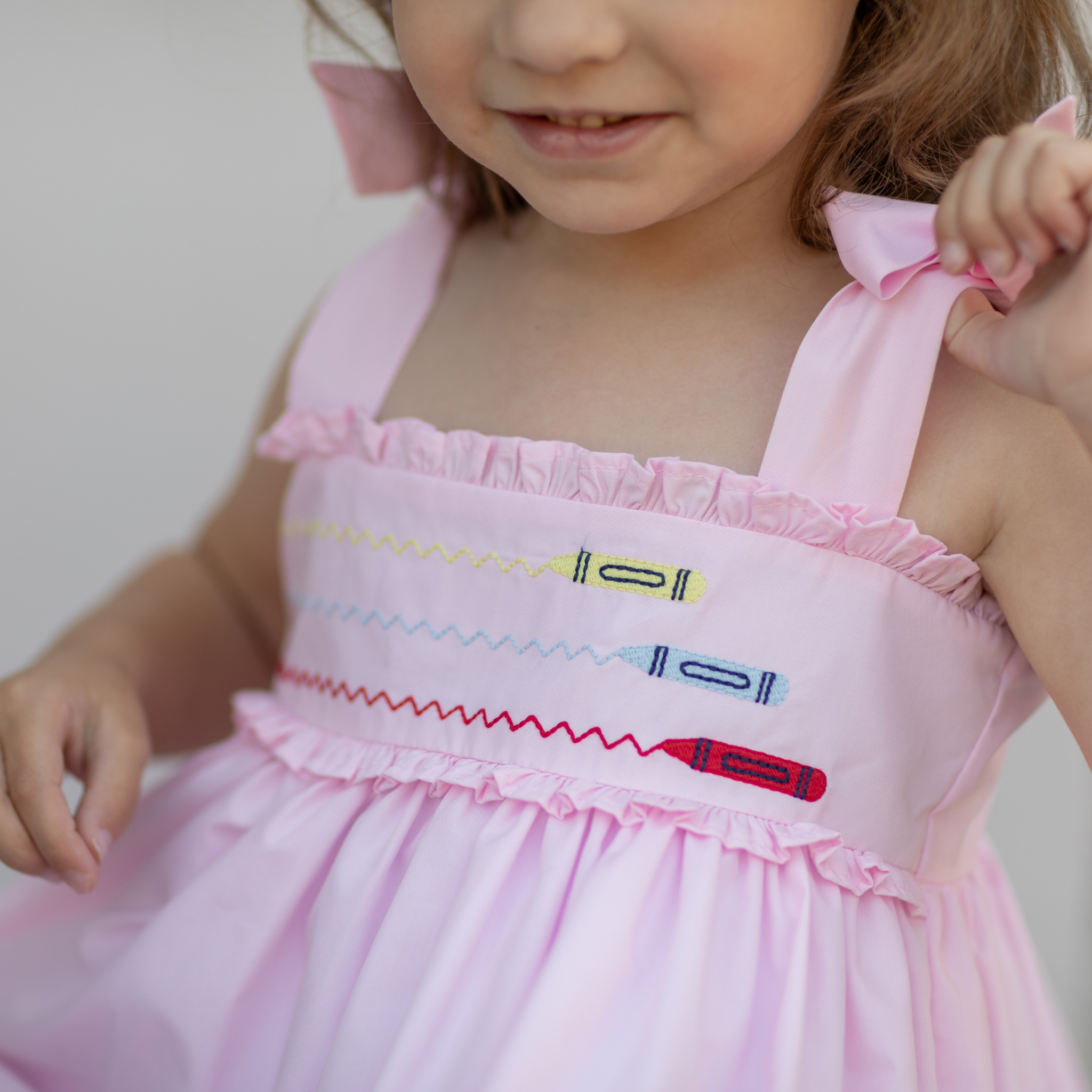 Henry Duvall Daisy Dress in blush pink cotton with hand-smocked crayon embroidery and shoulder bow ties, classic girls back-to-school dress for first day of school photos and fall occasions.