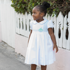 Henry Duvall Eloise Dress in white cotton with Bailey’s Bay Blue trim and hand-smocked sailboats, classic heirloom baby girl summer outfit with scalloped Peter Pan collar