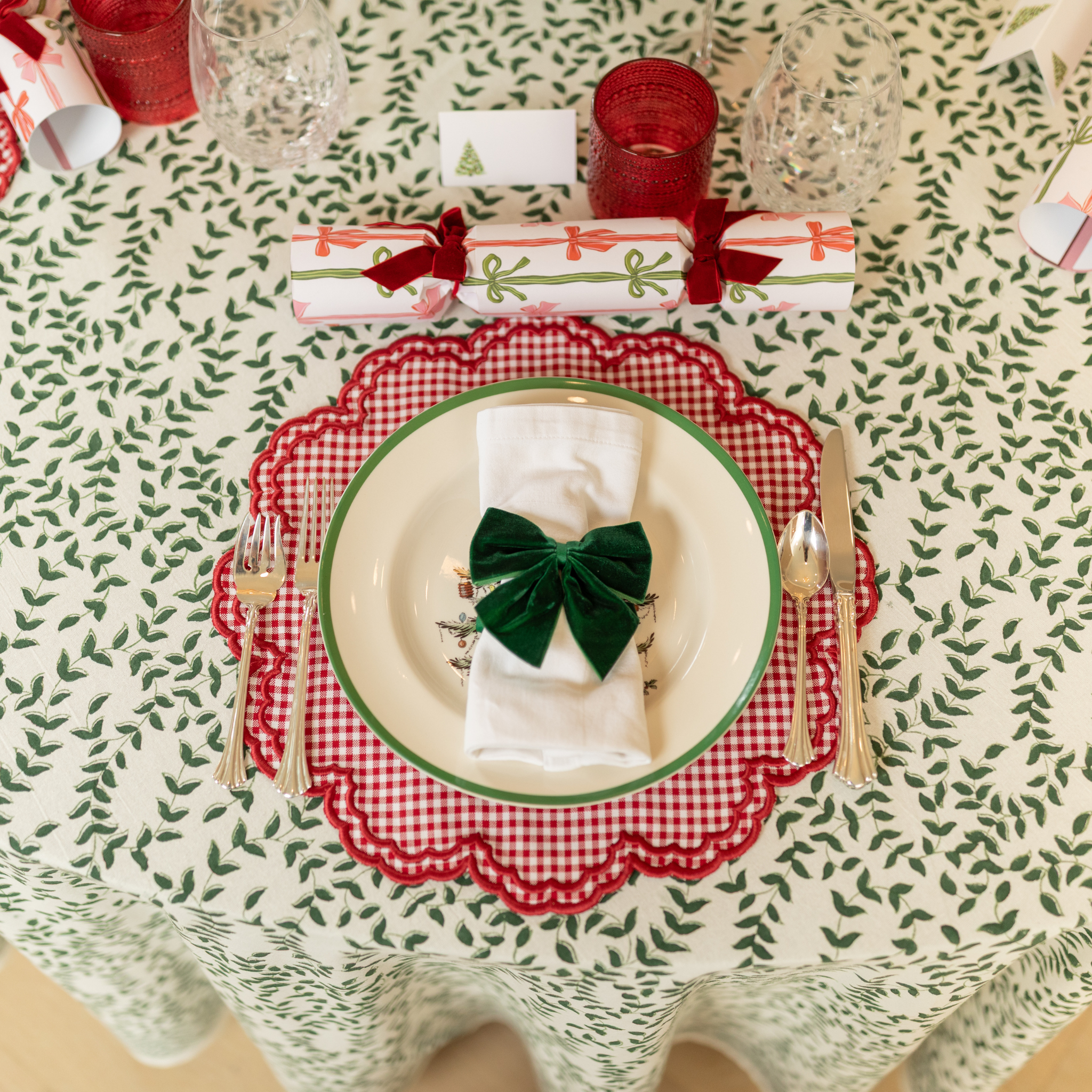 Holiday tablescape with Flying Sheep Country green leaf block-printed tablecloth, red ribbon details, holiday crackers, crystal glassware, and a white floral centerpiece