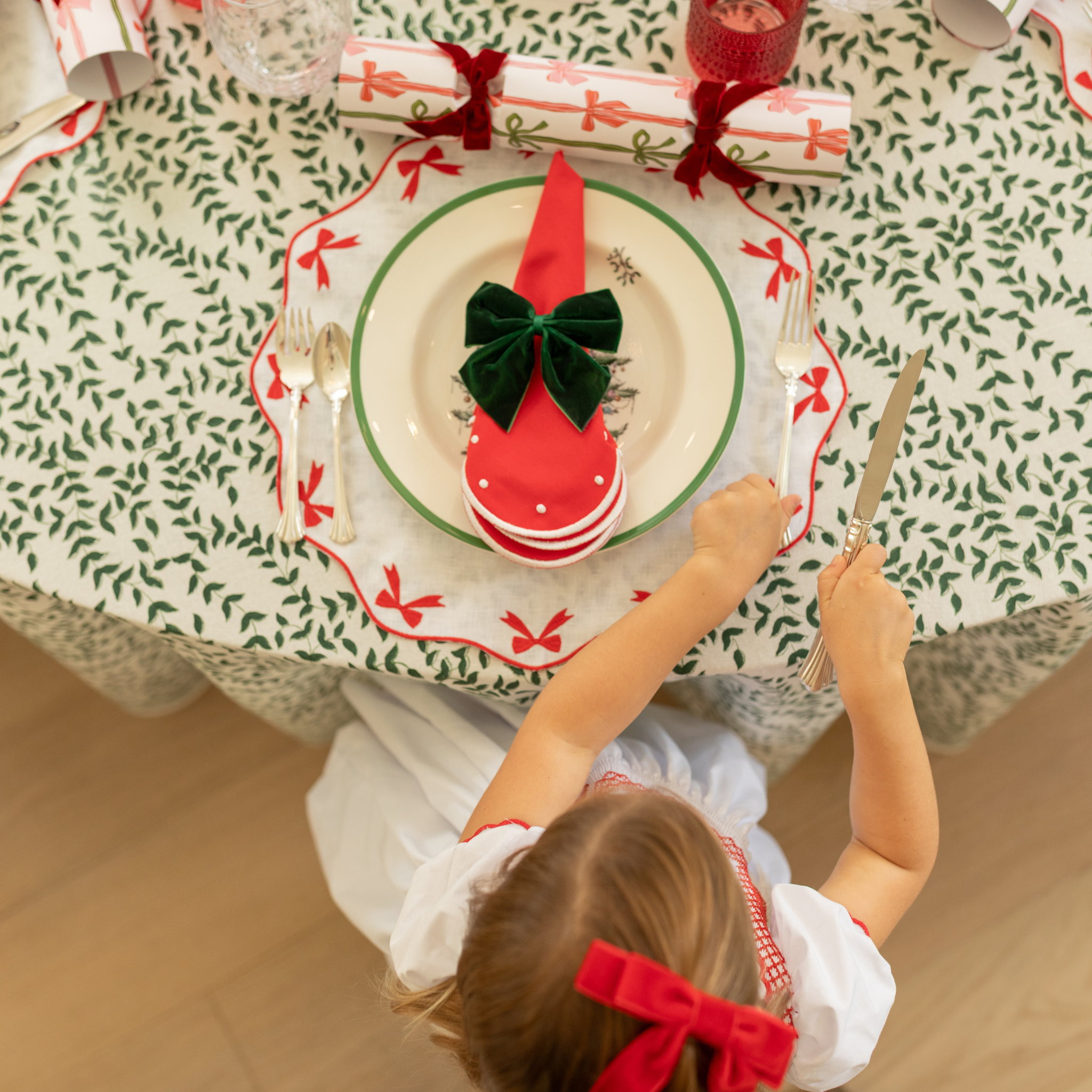 Holiday tablescape with Flying Sheep Country green leaf block-printed tablecloth, red ribbon details, holiday crackers, crystal glassware, and a white floral centerpiece